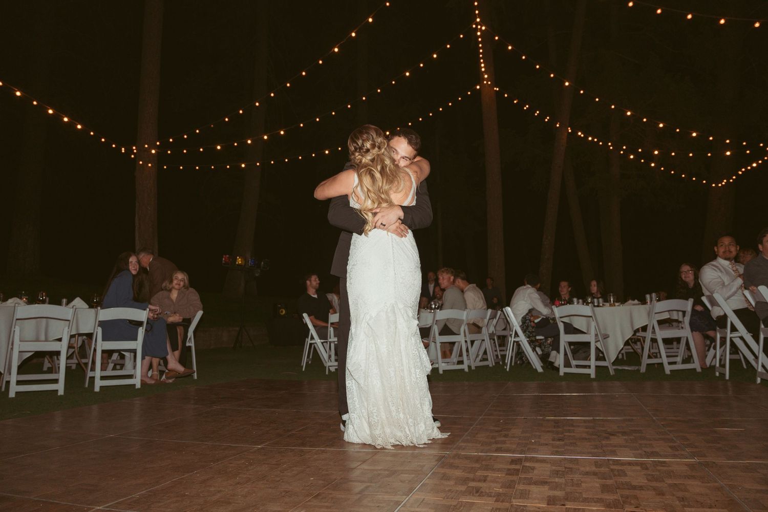 Outdoor wedding reception setup with white chairs and string lights creating a romantic atmosphere.