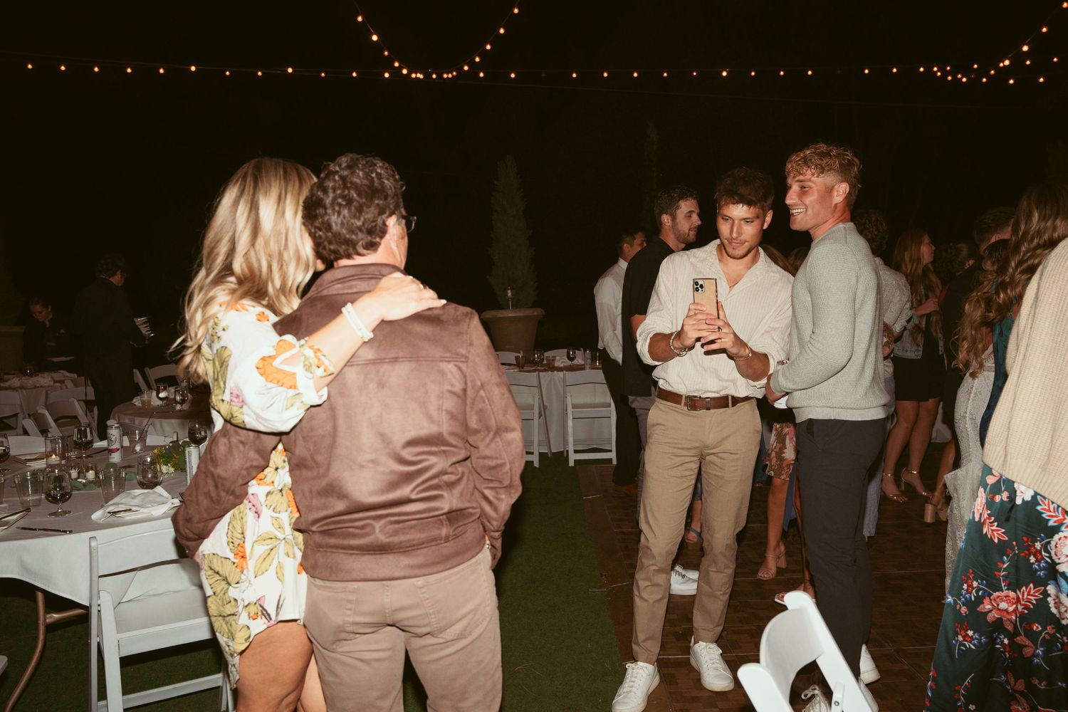 Couples slow dancing together on an outdoor dance floor at a nighttime wedding reception.
