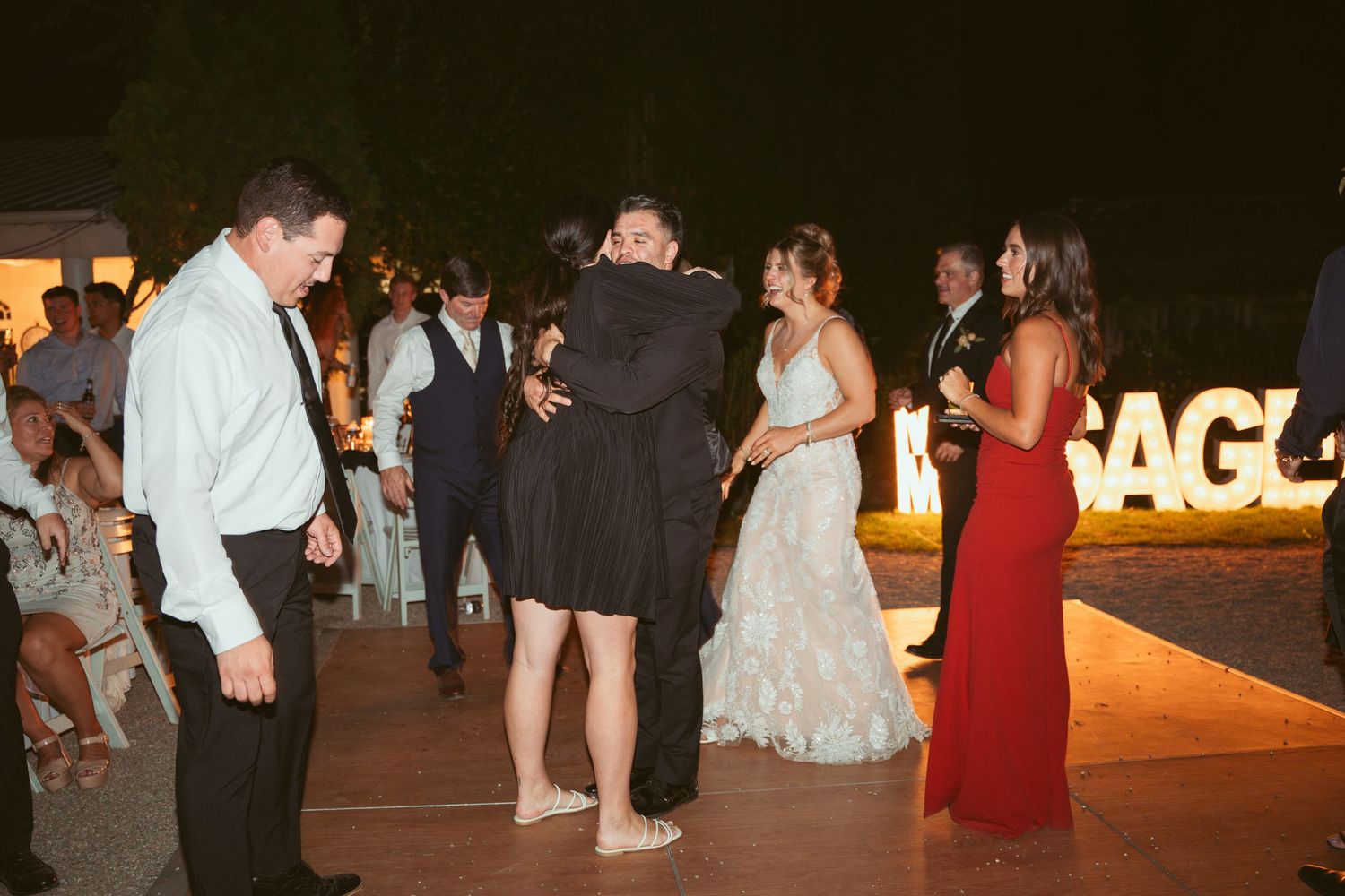 Couples dancing at an evening outdoor wedding reception with lit signage.