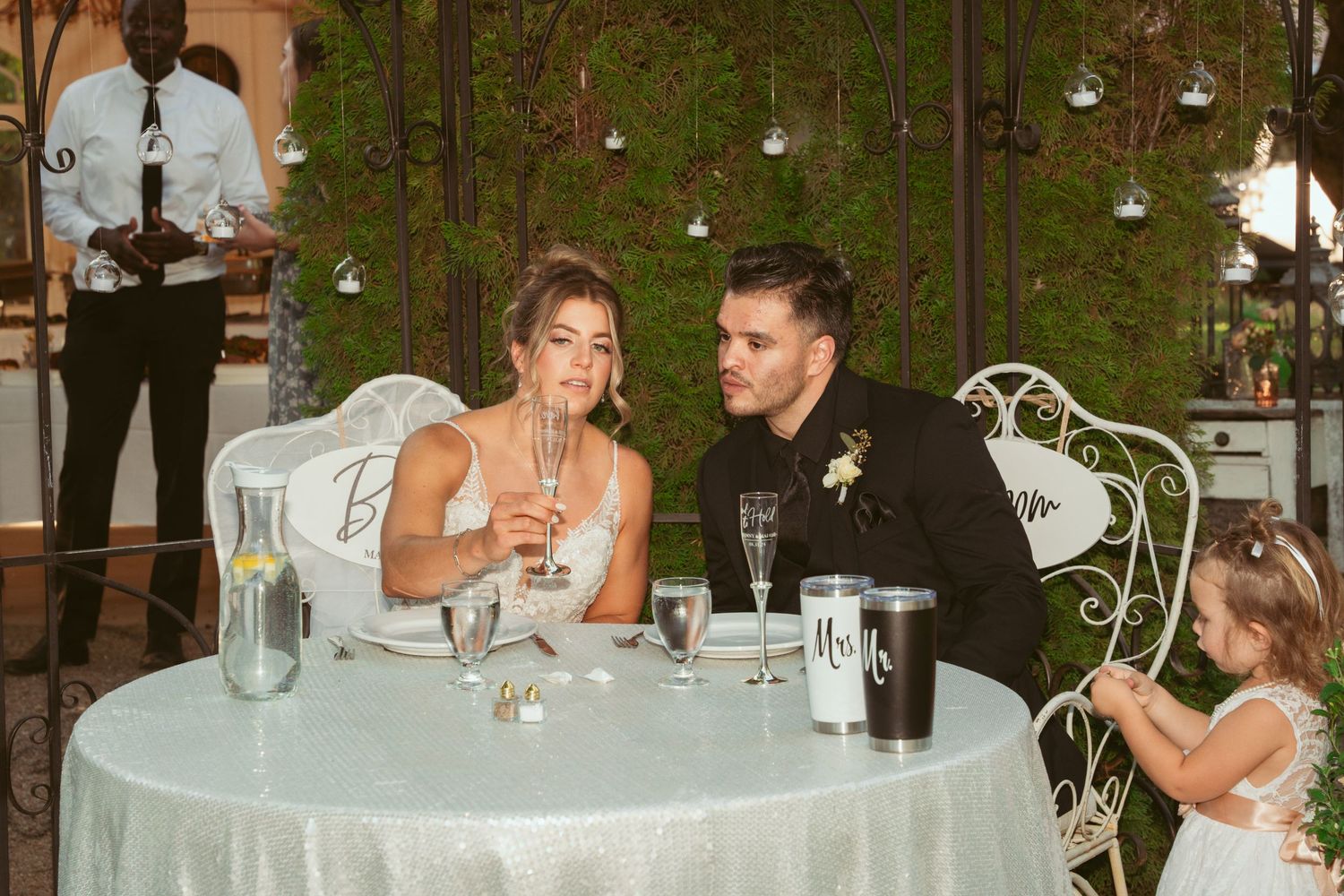 Newlyweds sharing a private moment at their reception table with champagne under hanging lights.