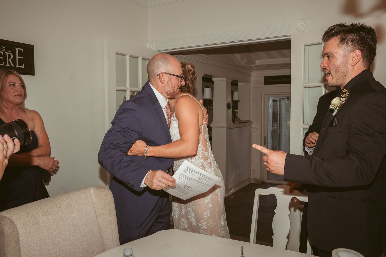 Indoor wedding reception with guests dancing and celebrating in a dimly lit room.
