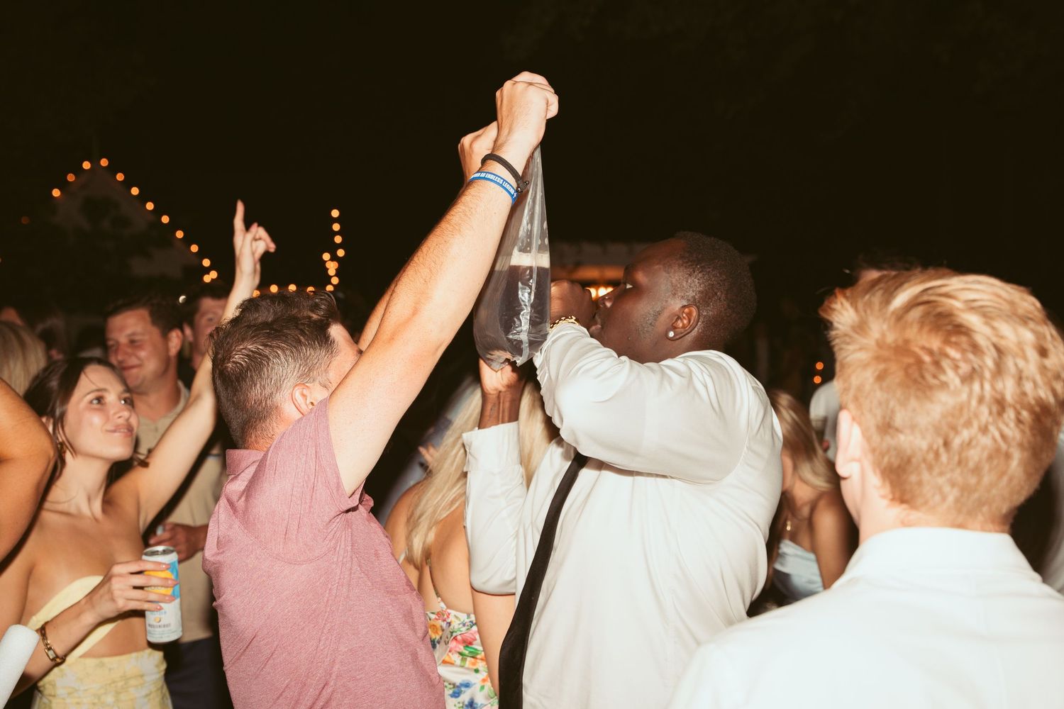 Enthusiastic party guests raising drinks and celebrating during a lively nighttime reception.