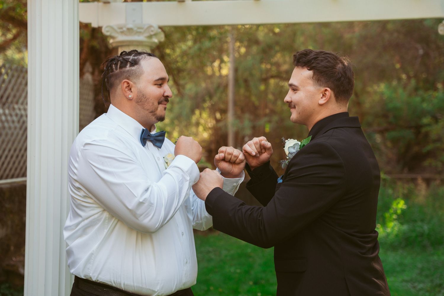 Groomsmen and bride celebrate with playful fist bumps under a white pergola.
