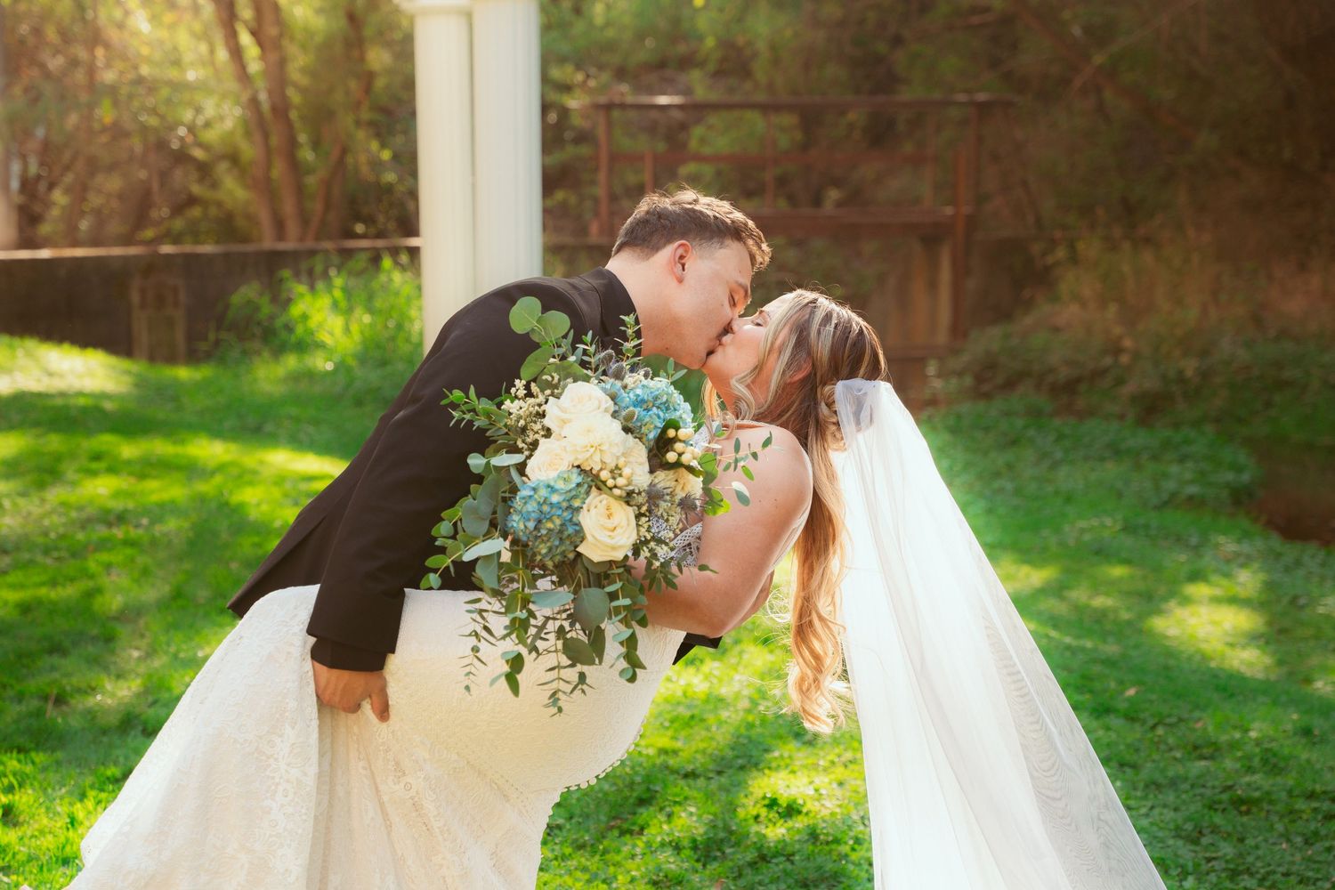 Couple shares intimate moment under white garden pergola during sunset wedding ceremony.