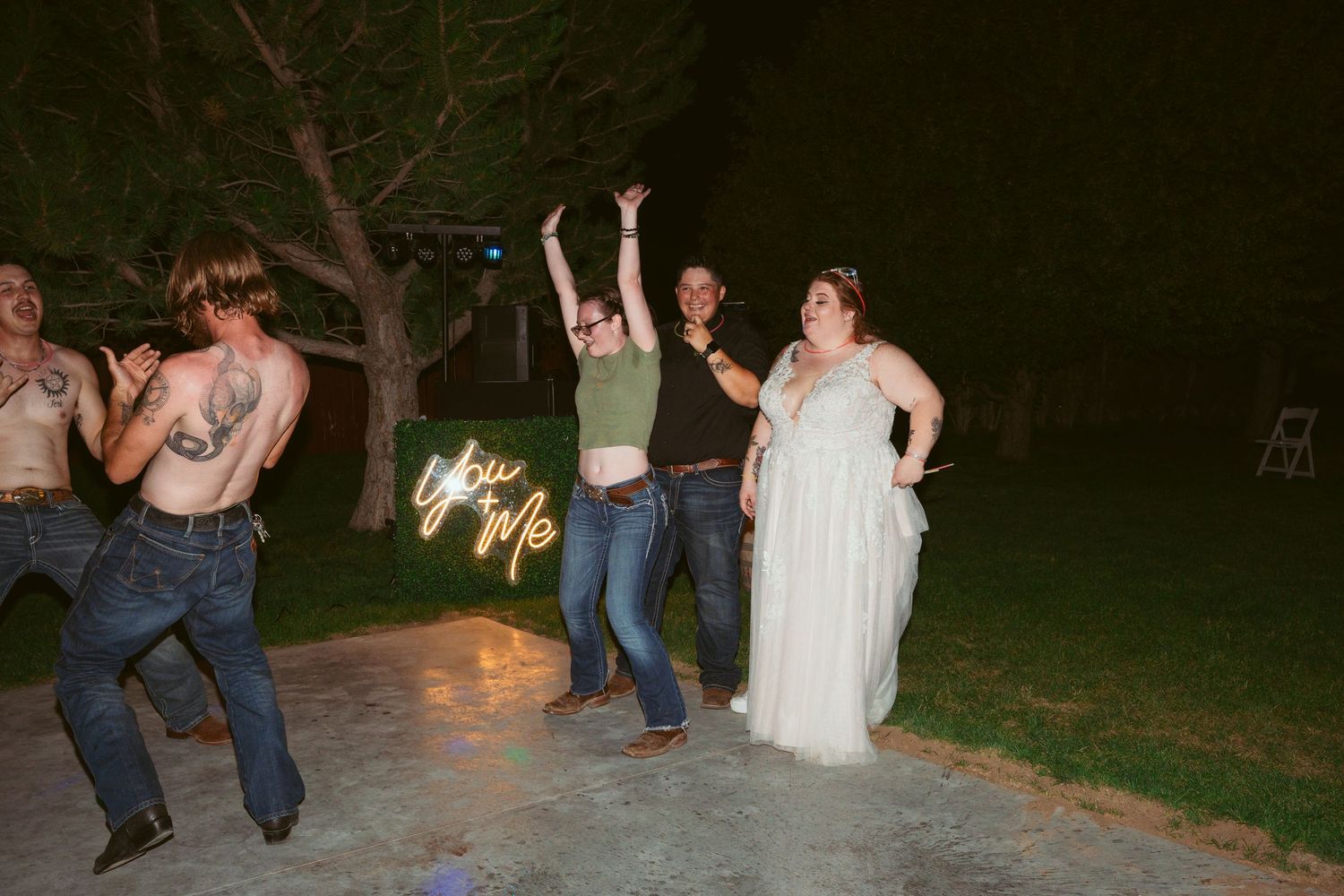 Wedding party dancing and celebrating on outdoor patio at night.