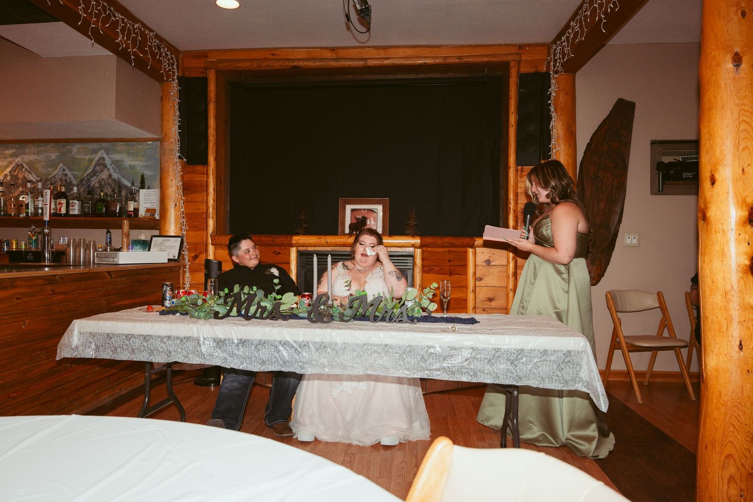 Wedding reception setup with long head table adorned with greenery and wooden decor elements.