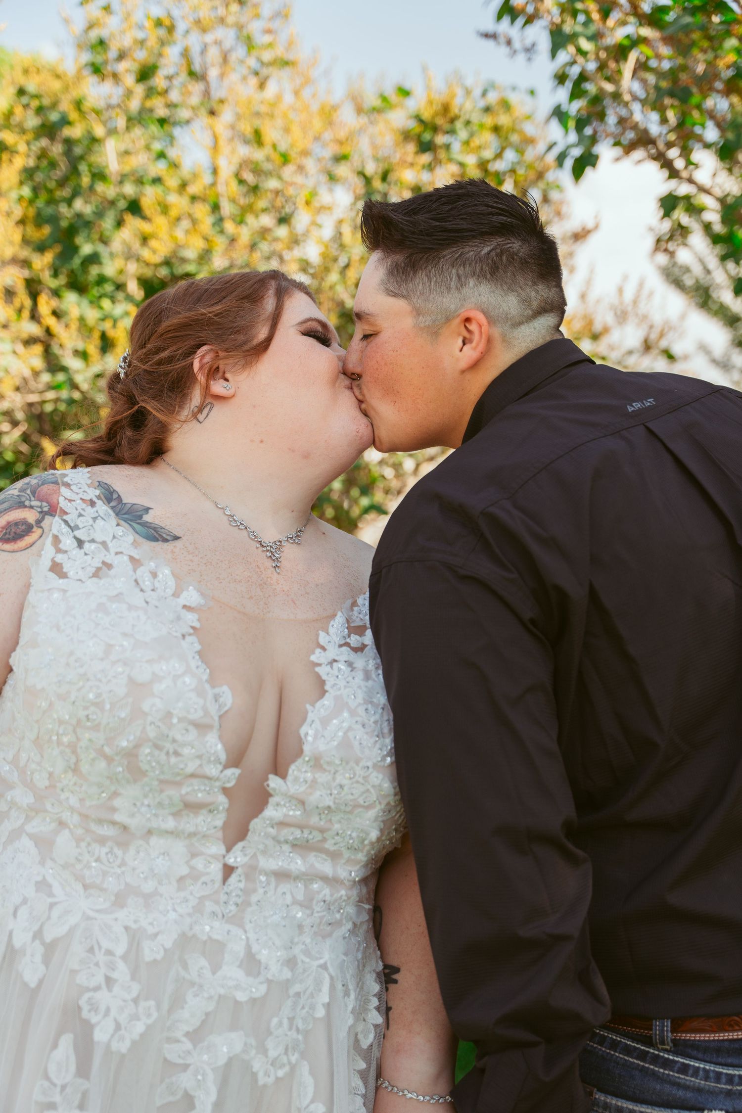 A romantic wedding kiss between newlyweds outdoors with autumn foliage in the background.