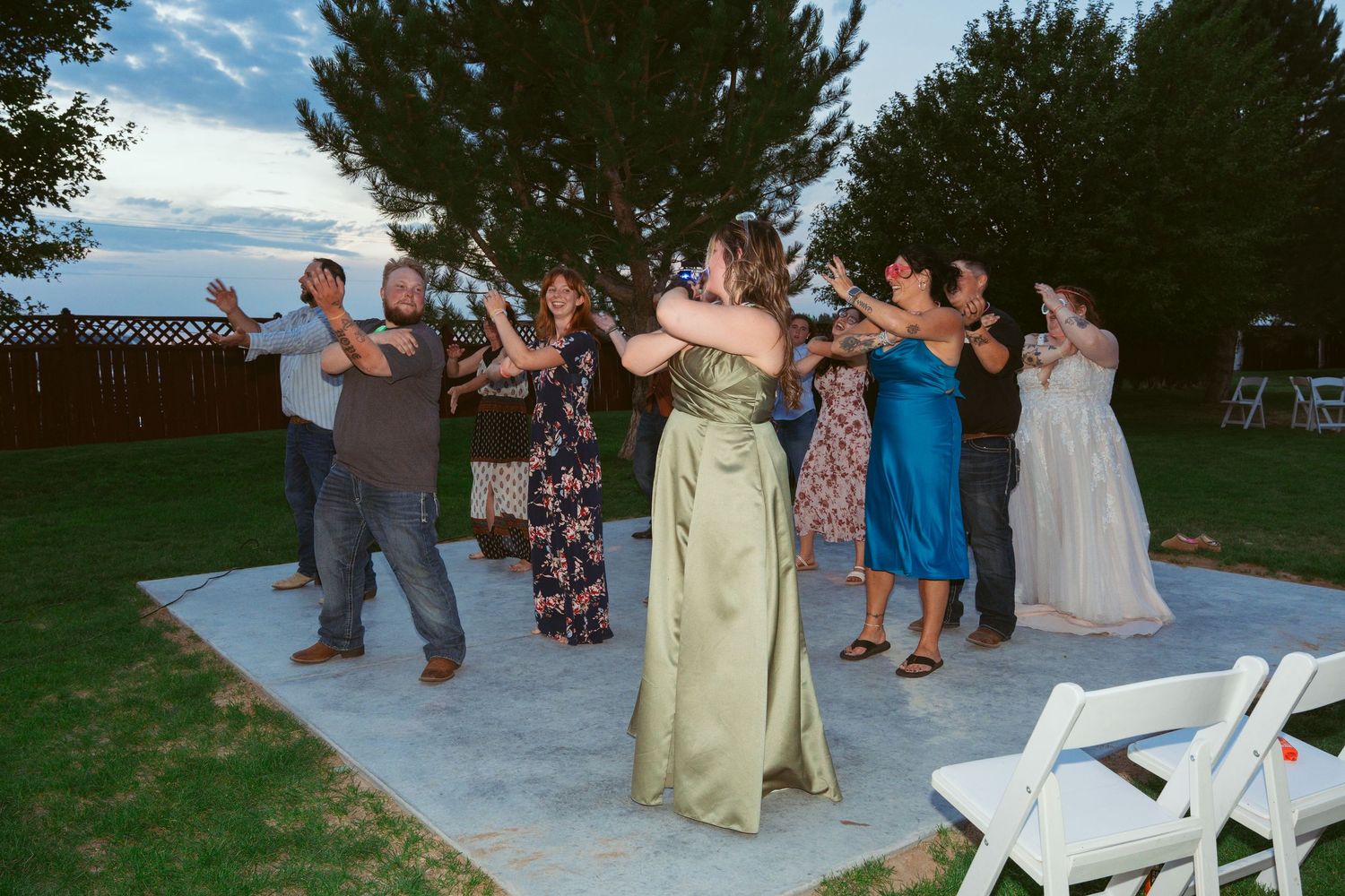 Wedding guests dance in a line on an outdoor patio during daytime celebrations.