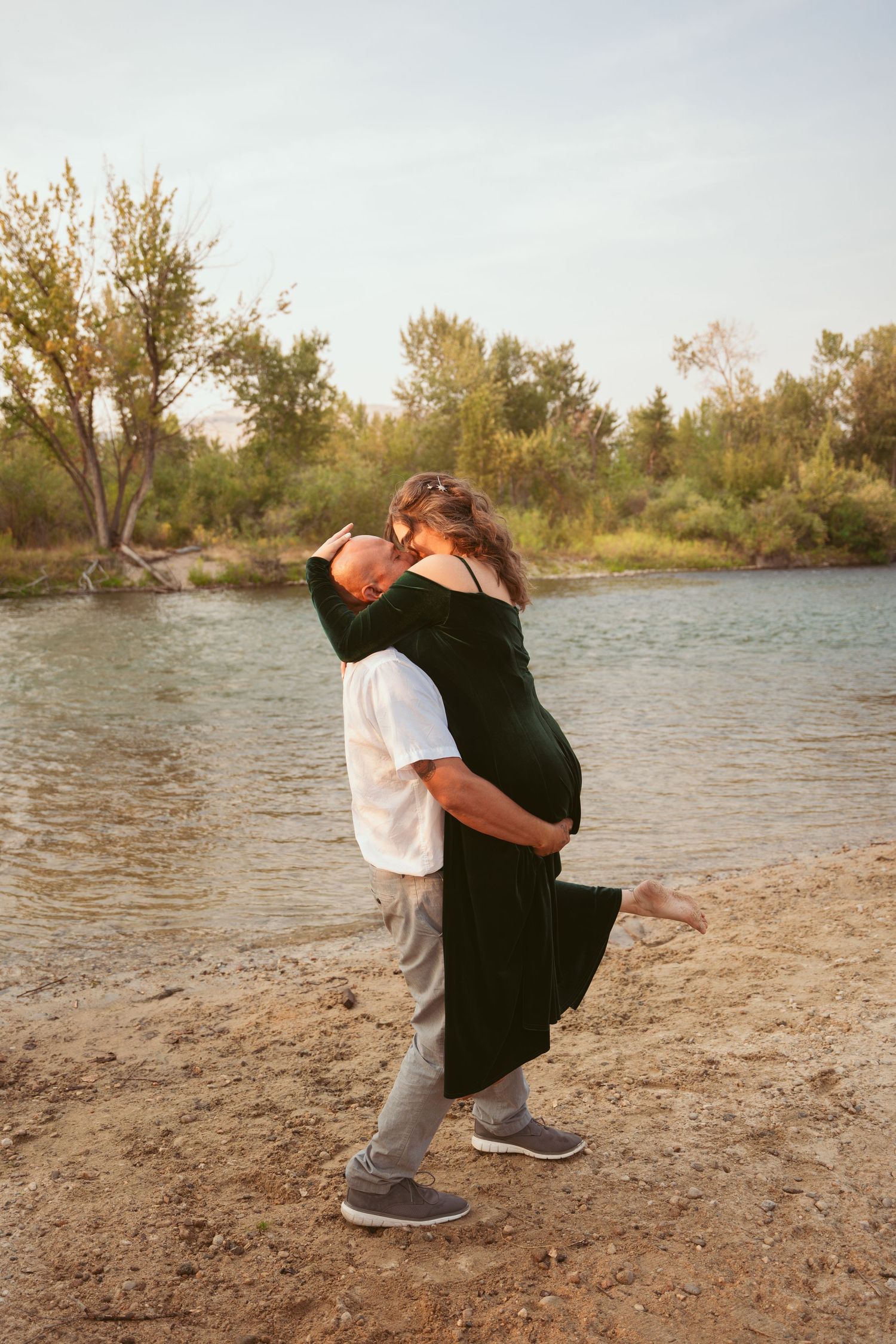 A playful couple dances and spins together on a beach during sunset.