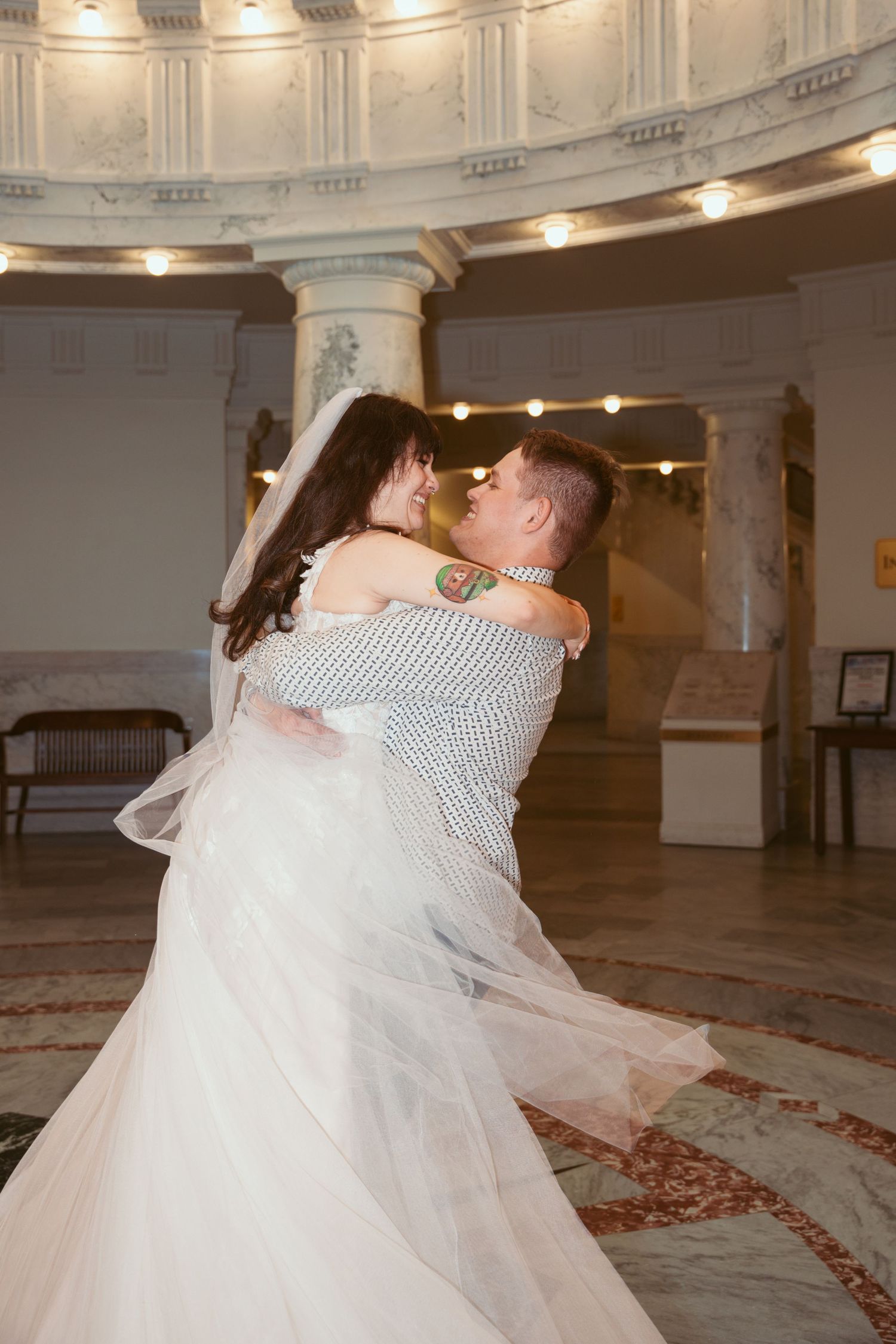 A couple dances together in a grand ballroom with ornate architectural details and warm lighting.