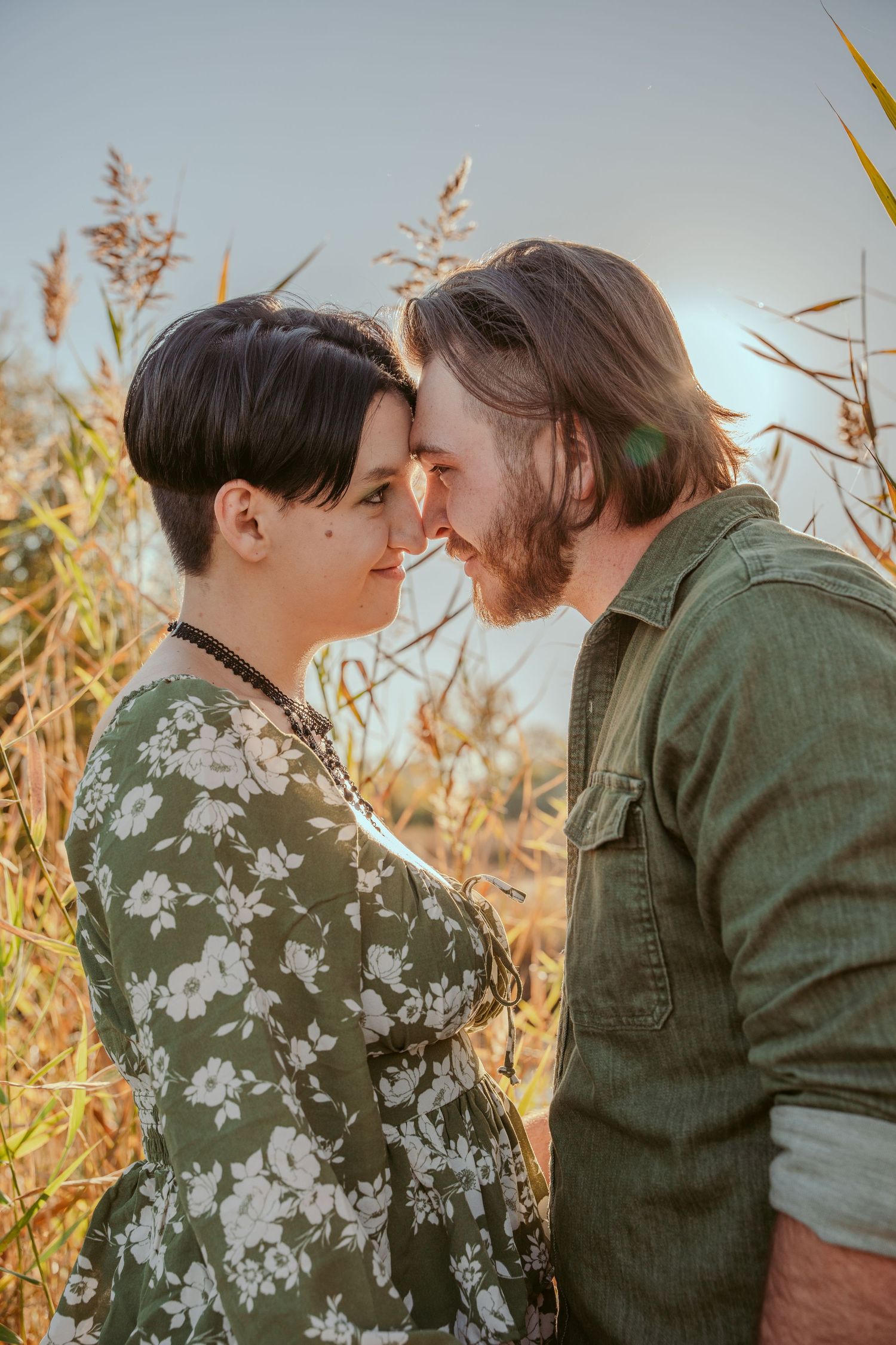 A romantic couple embraces in golden sunlight among tall reeds wearing green clothing.