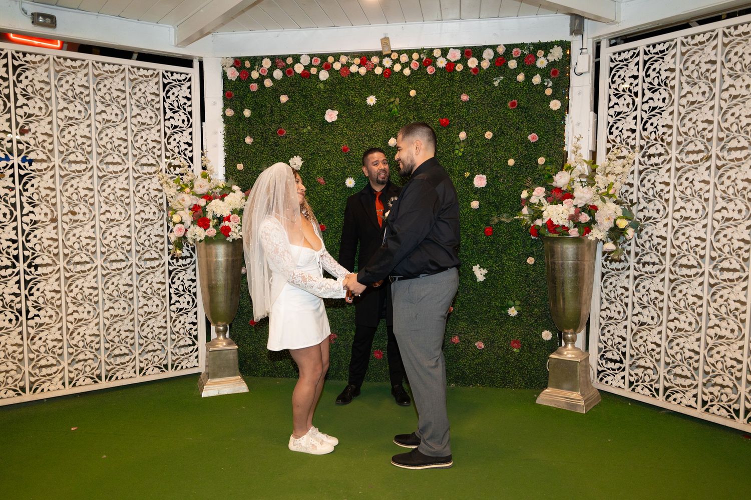 Couple dancing in front of a green wall decorated with white panels and string lights at a wedding venue.