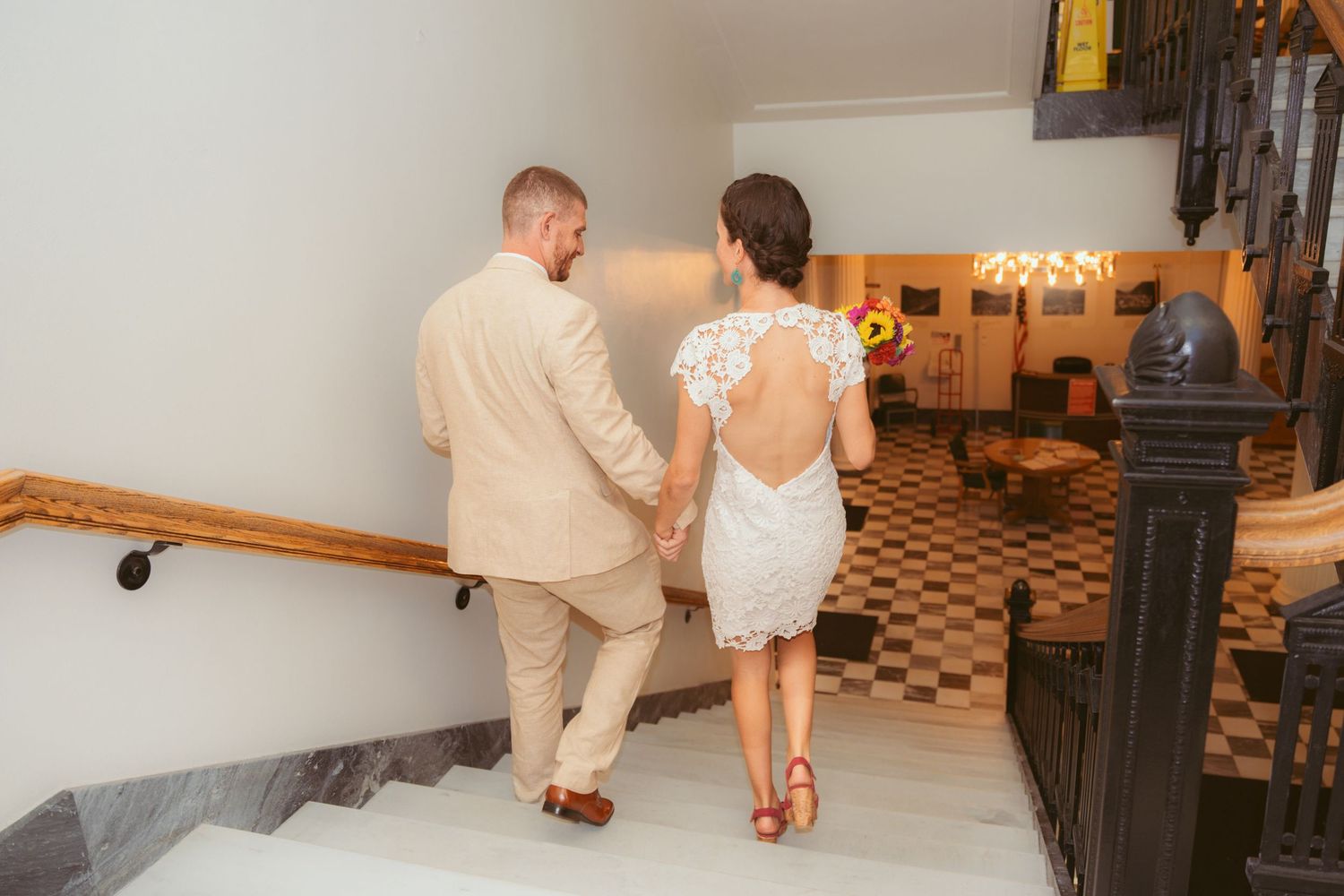 A couple walks hand in hand through an elegant hallway with checkered floors.