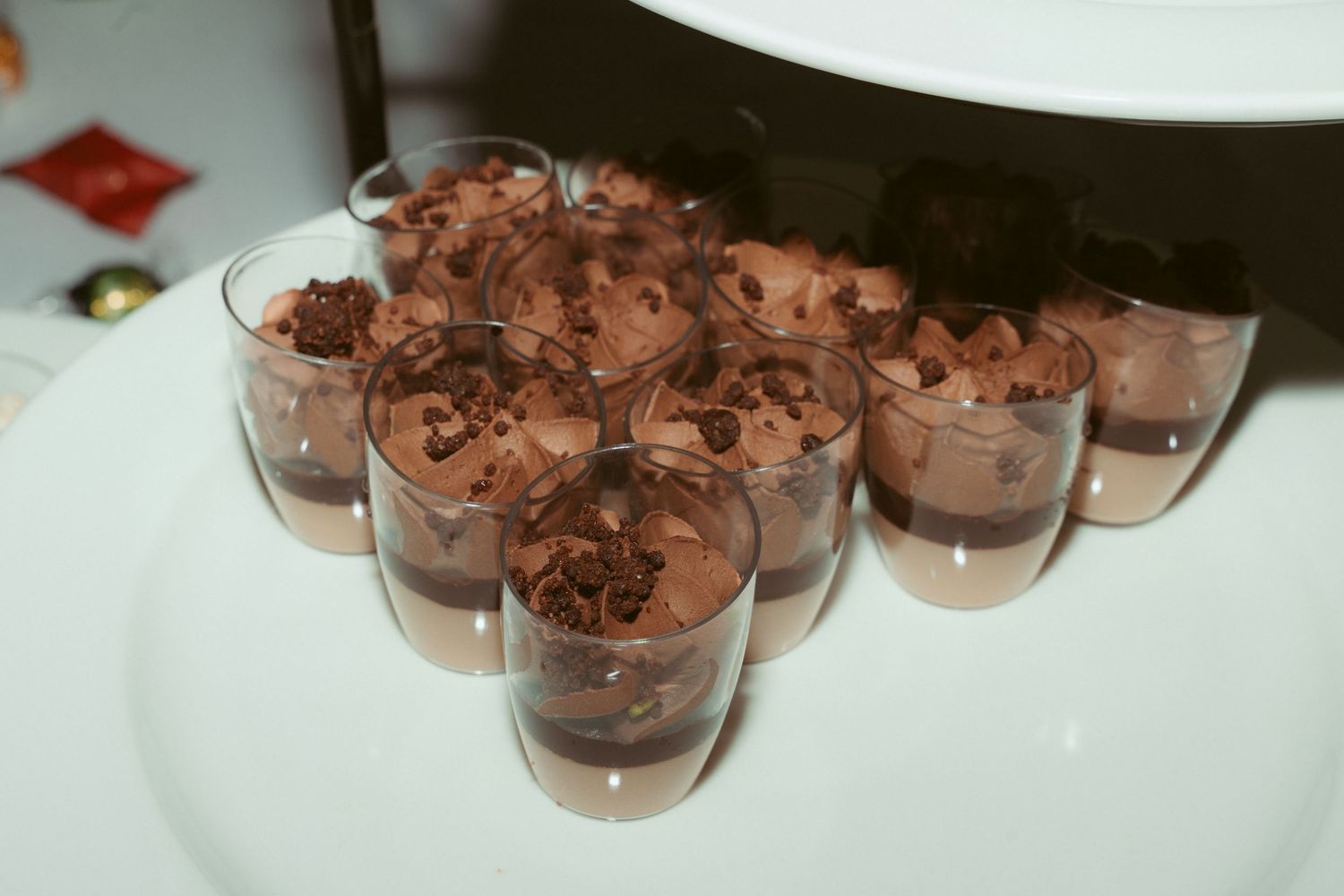 Row of chocolate mousse desserts in small glass cups displayed on white tablecloth.