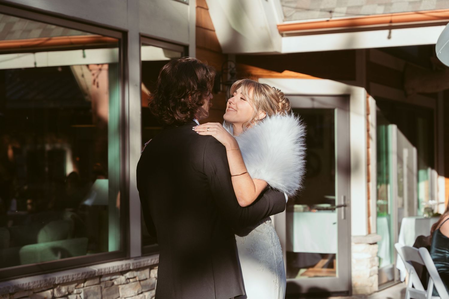 A romantic dance moment captured at an outdoor wedding reception with glass windows.