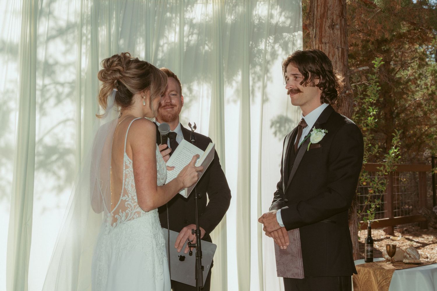 Forest wedding scene with white fabric backdrop and natural lighting through trees.