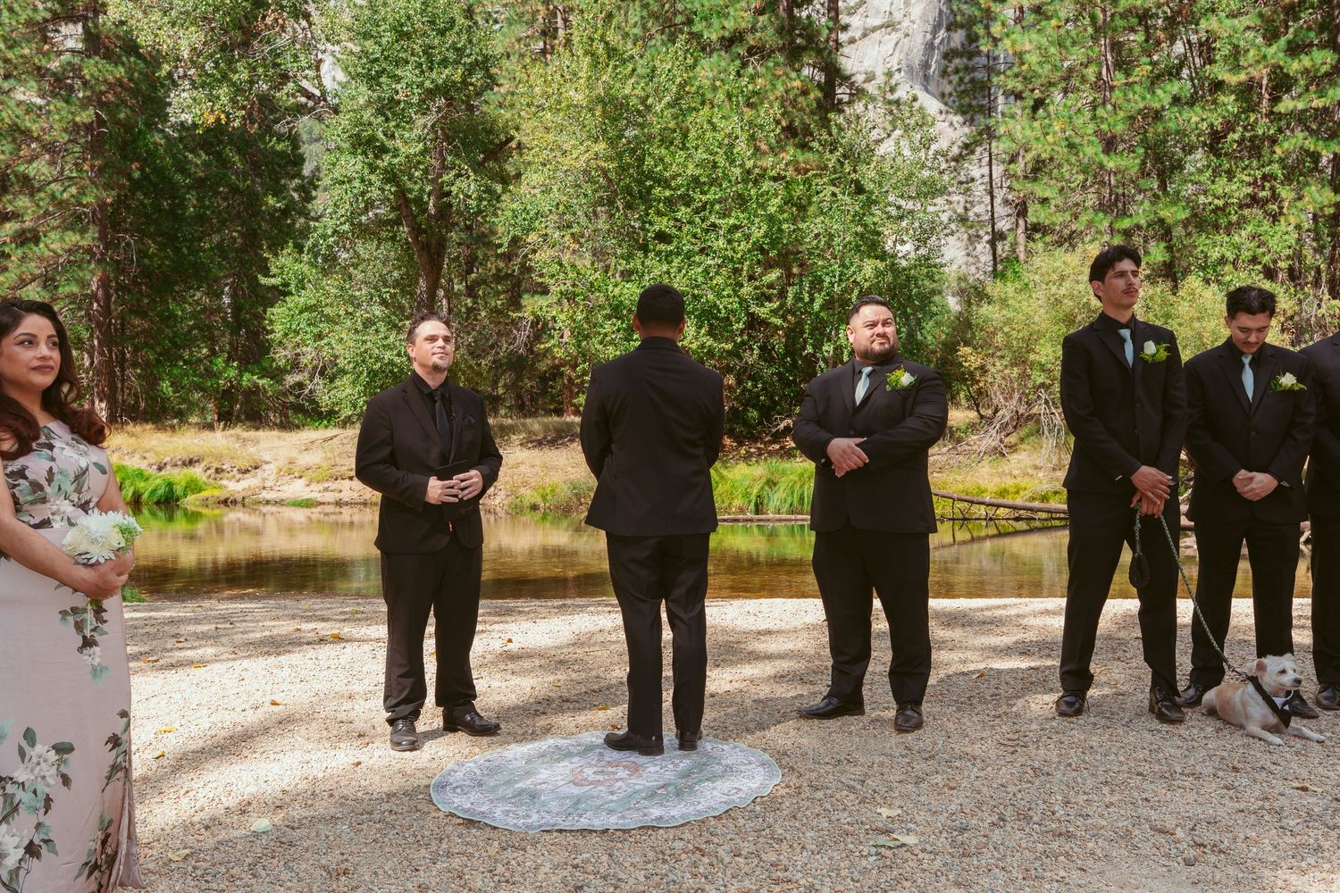 Wedding party in black attire standing in line at outdoor Yosemite venue with trees in background.