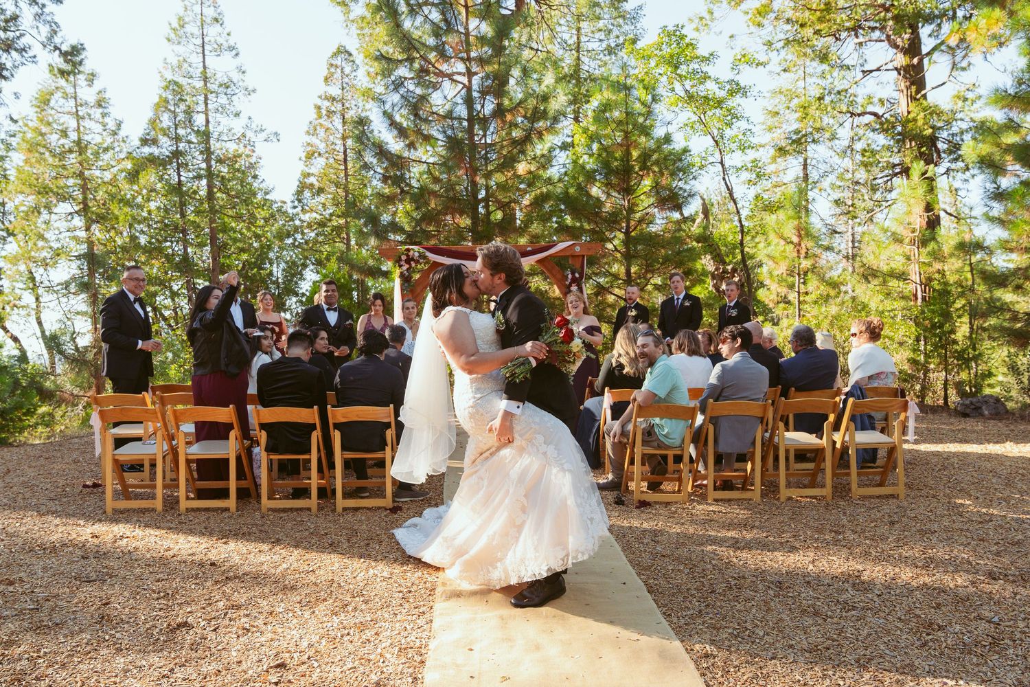 Panoramic view of forest wedding ceremony with wooden chairs and natural surroundings.