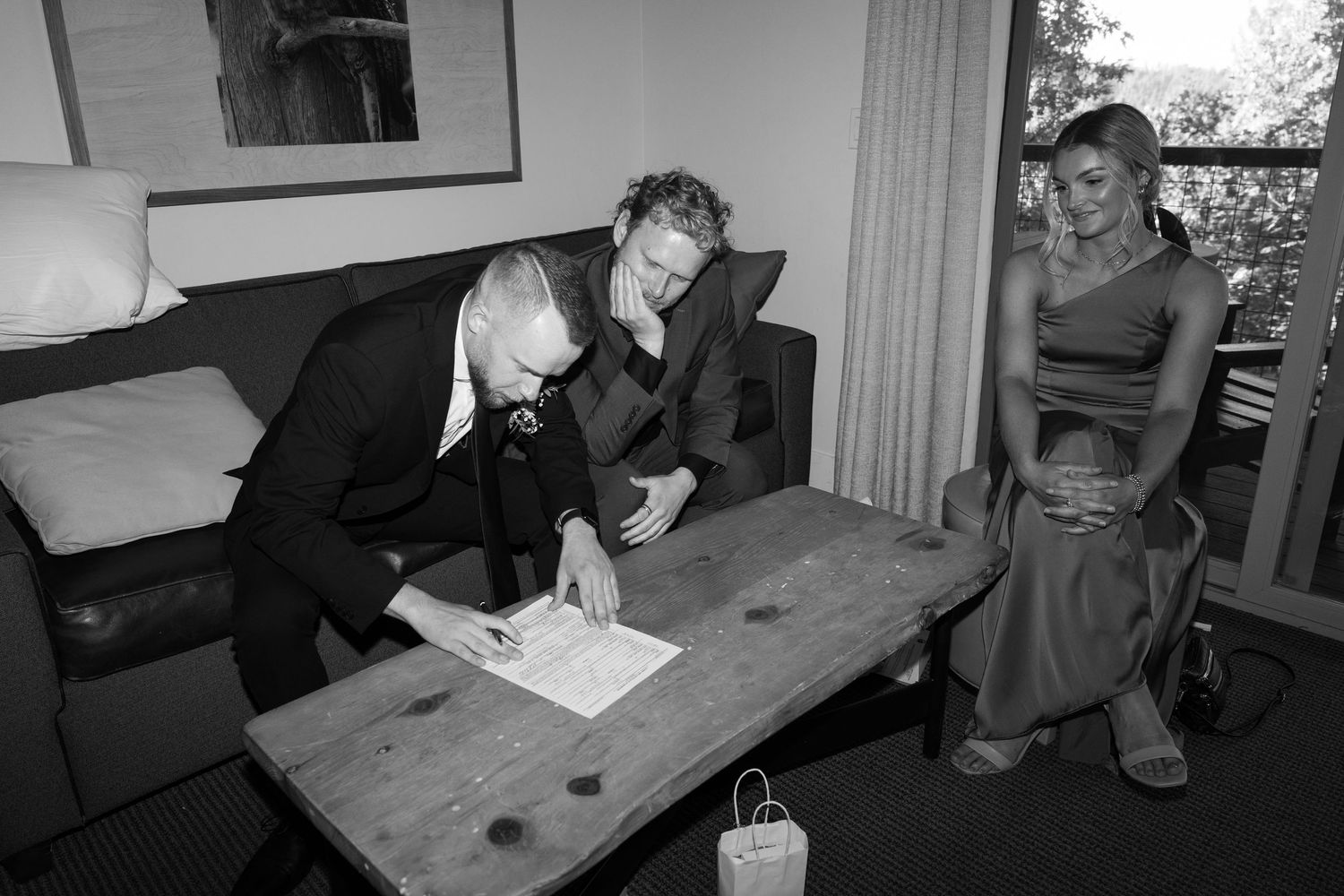 Wedding party members sign official documents at a wooden table indoors.