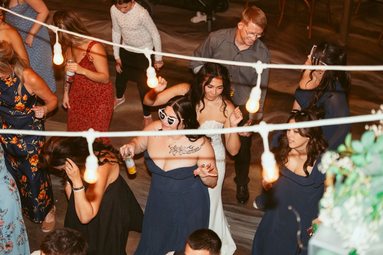 Wedding reception guests dancing and mingling under decorative string lights.