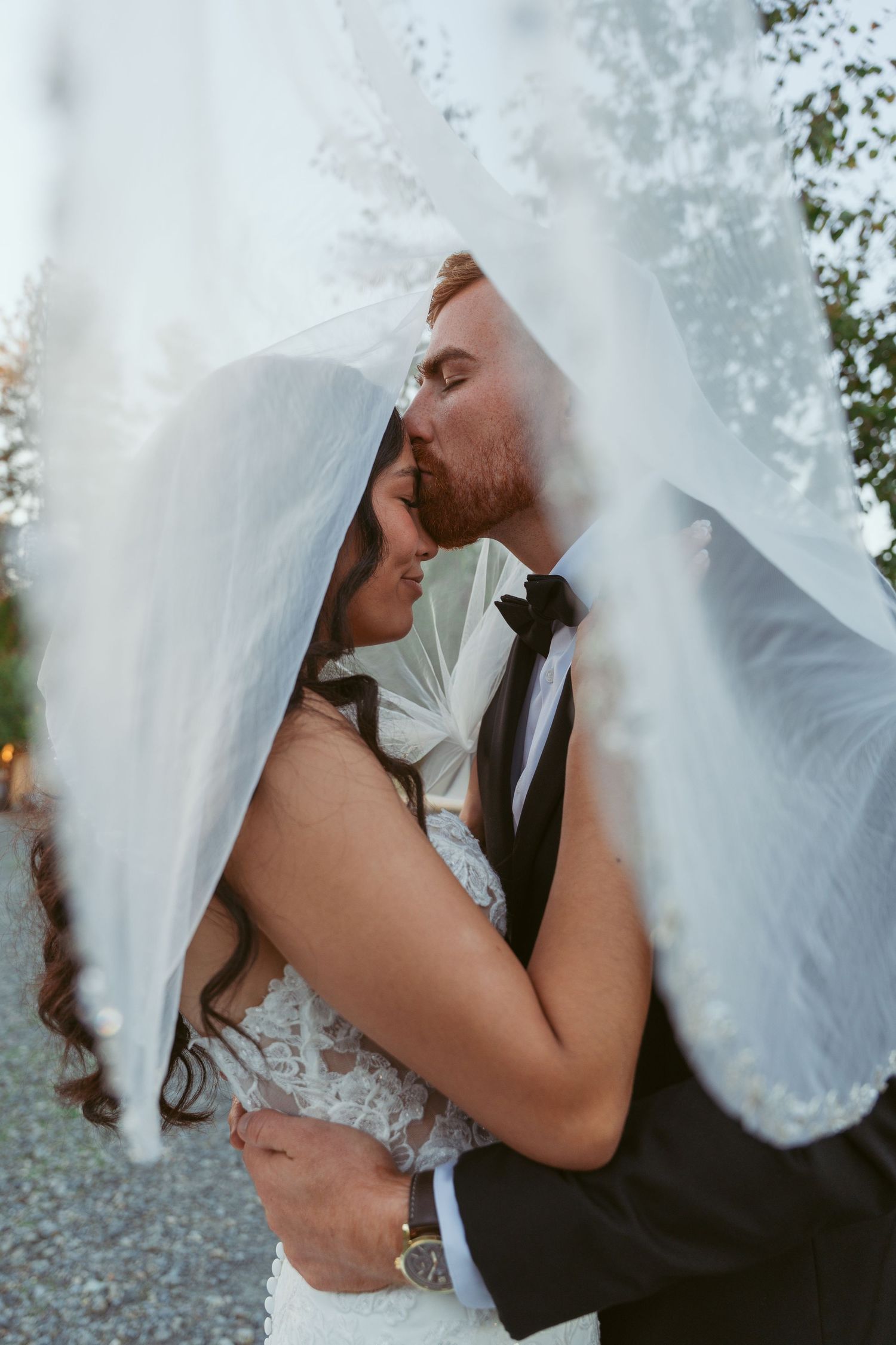 Close-up shot of romantic kiss under flowing white wedding veil.