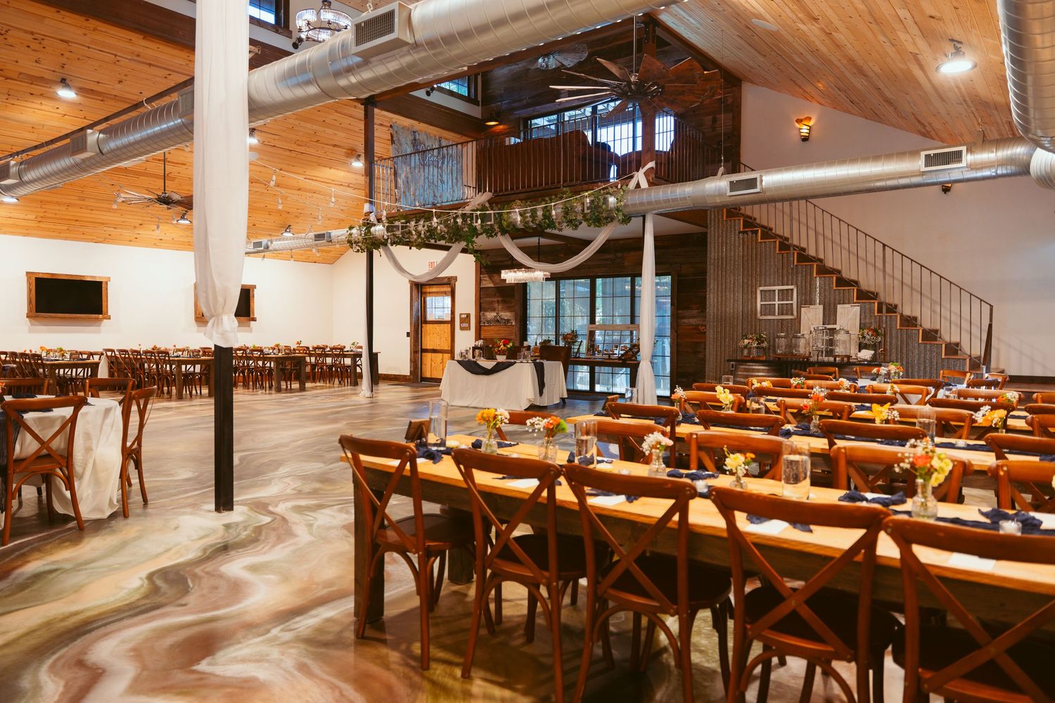 Modern rustic wedding reception venue with wooden tables and ceiling beams.