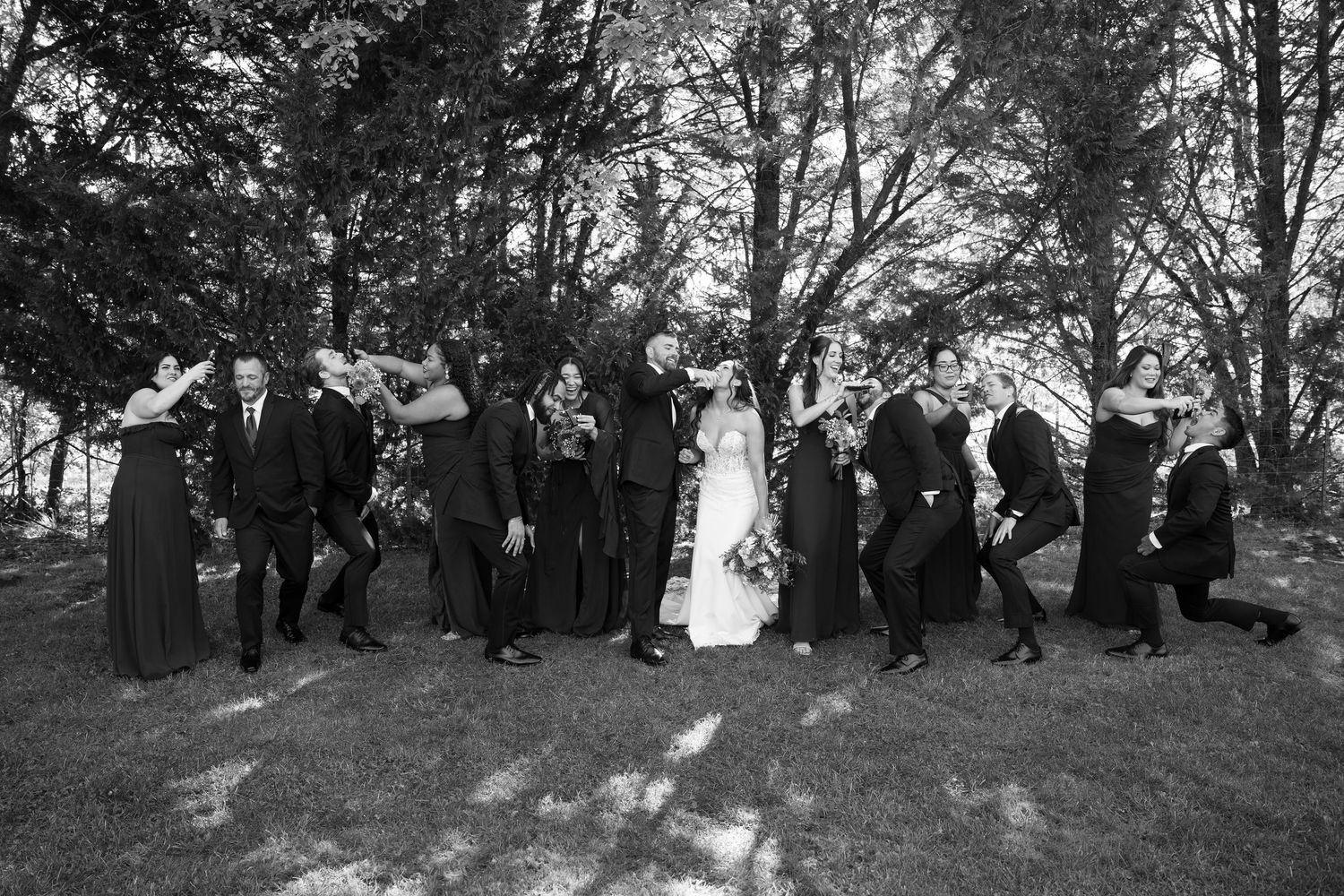 Black and white panoramic shot of wedding party posing on hillside under trees.