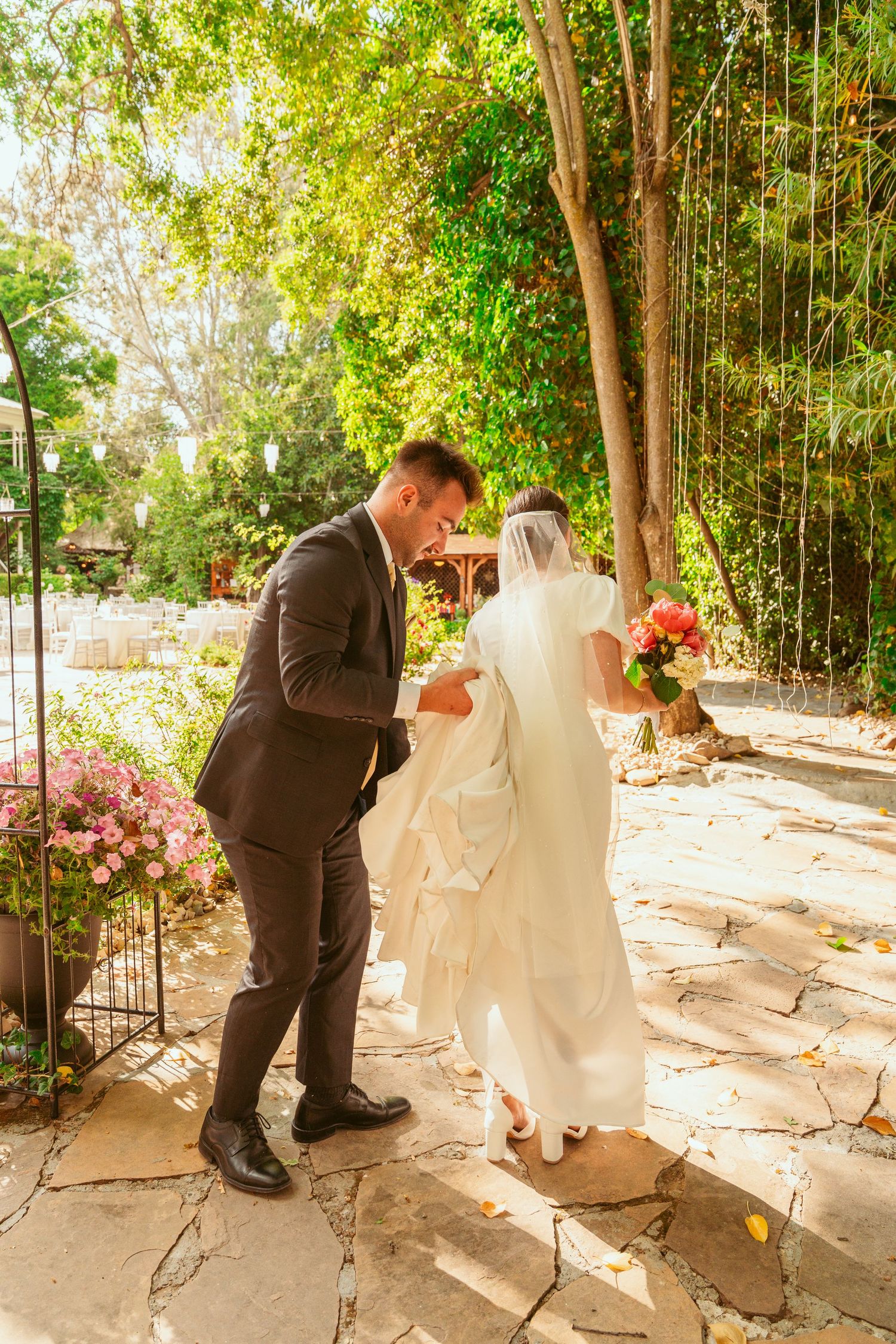 First look wedding photos being taken in a sunlit garden path with stone walkway.