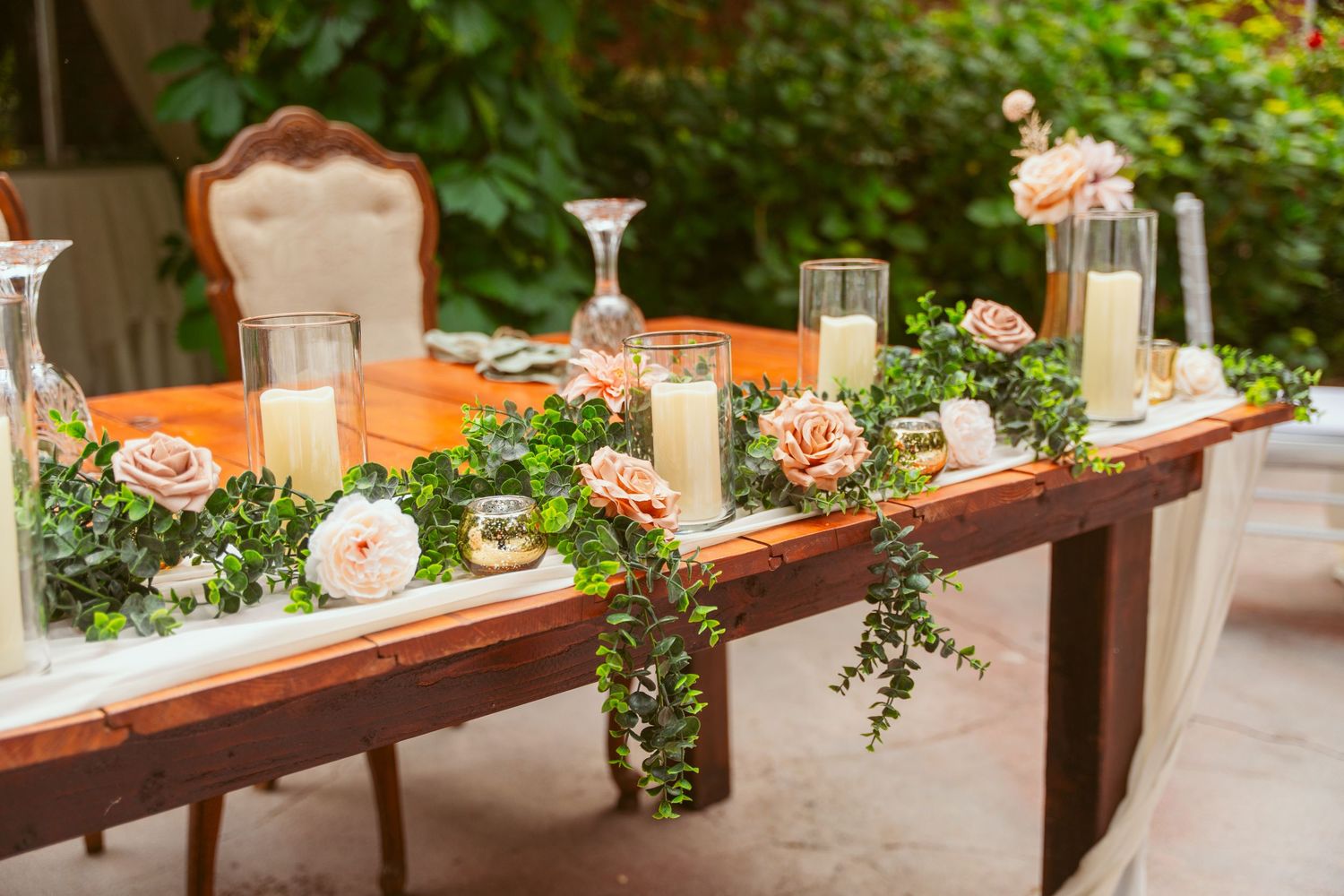 A decorated wedding reception table with floral centerpieces and candles in an outdoor setting.