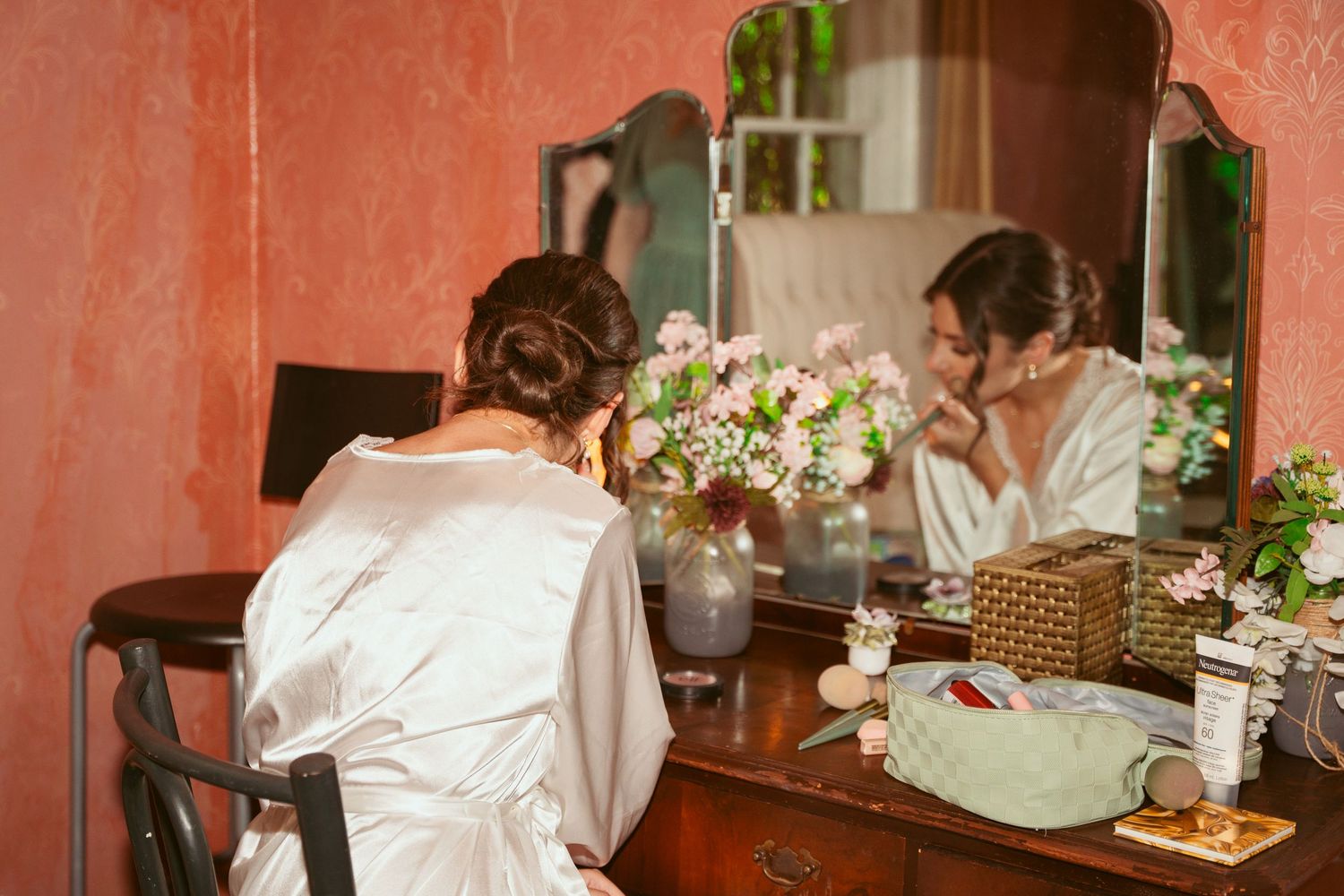 Antique wooden vanity with trifold mirror and fresh flower arrangements.