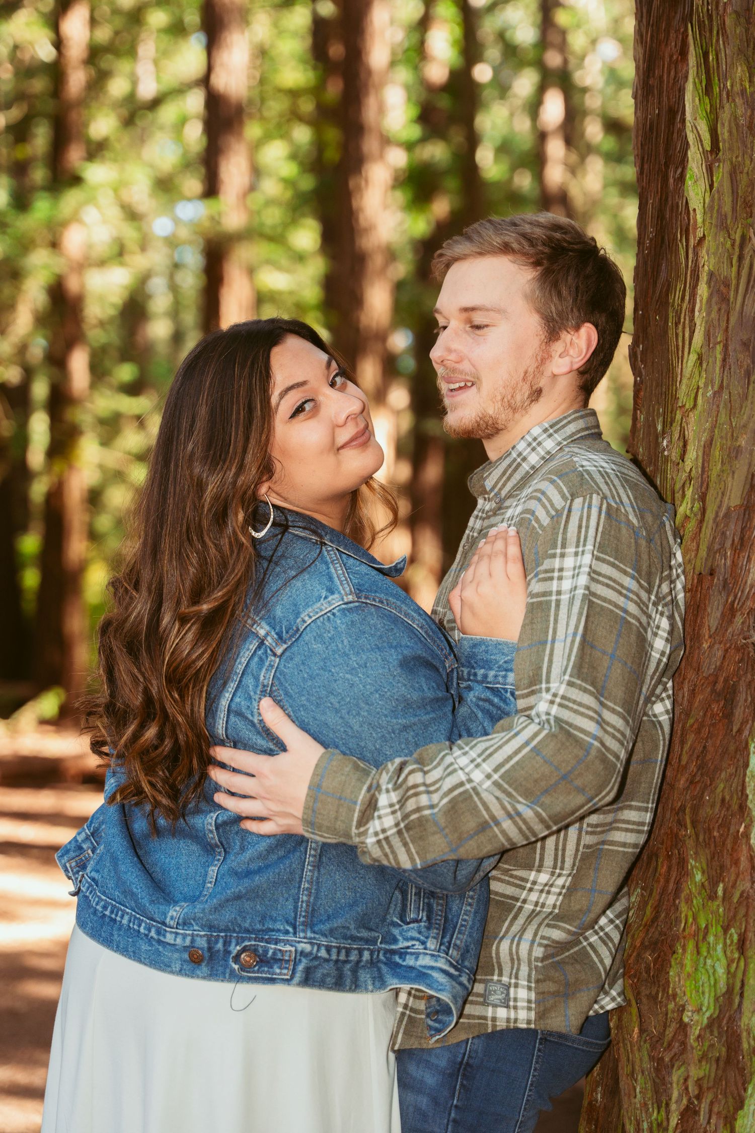 Romantic moment captured between two people among tall redwood trees in dappled sunlight.