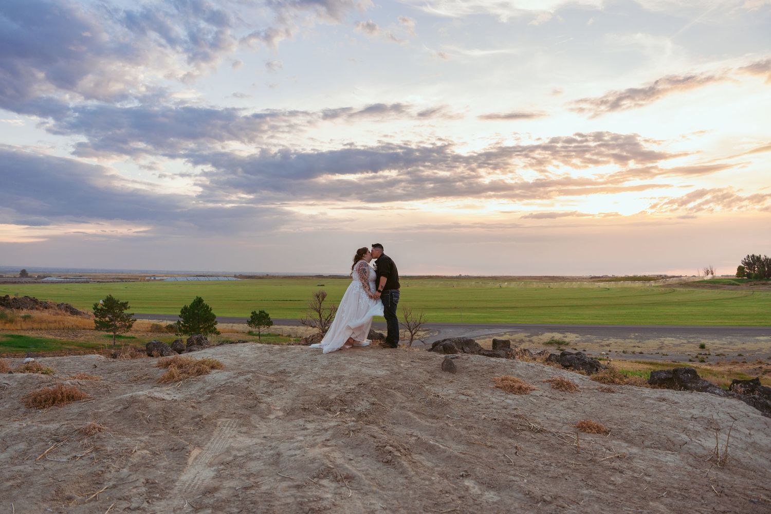 Wedding couple silhouetted against colorful sunset sky on rocky overlook with sweeping landscape views.