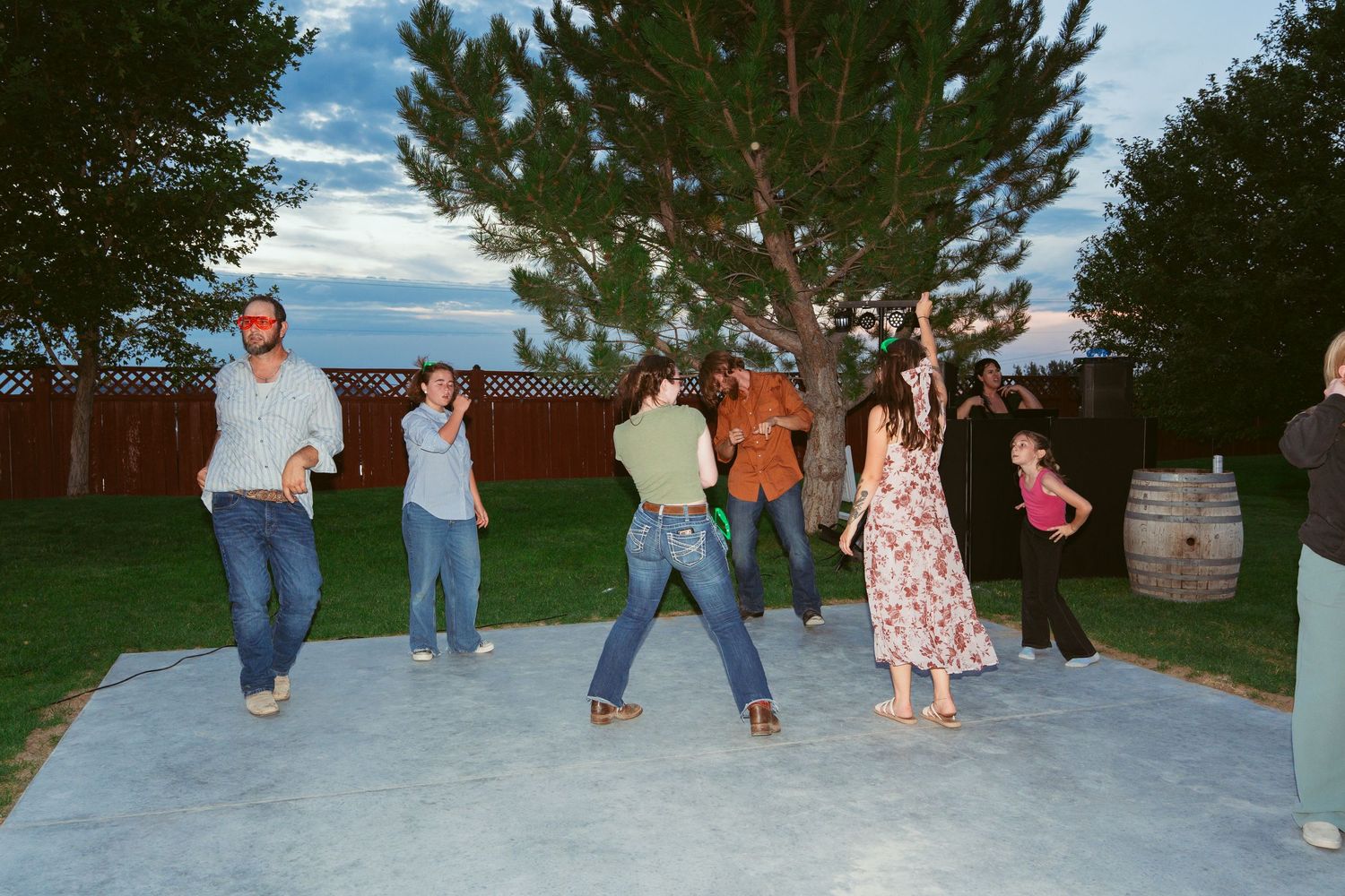 Dancers performing choreographed moves on an outdoor dance floor with trees in background.