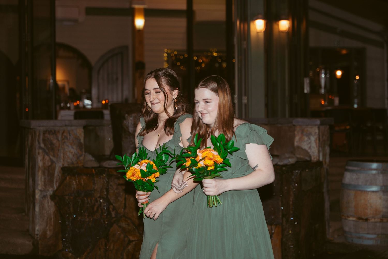 Wedding party members pose with colorful bouquets at an outdoor evening venue.