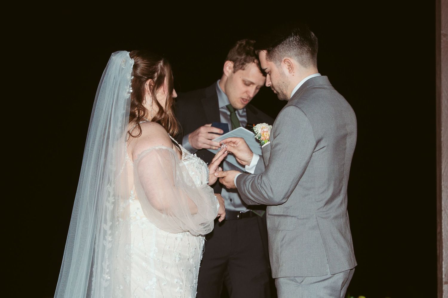 Couple during wedding ceremony at night under gazebo with floral decorations.
