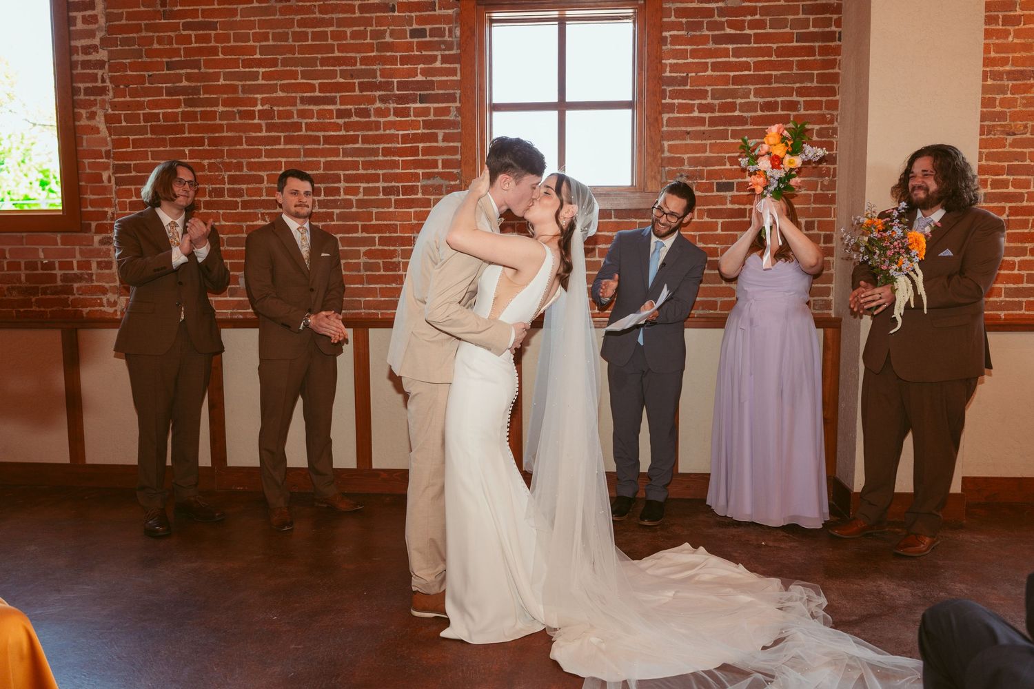 Wedding ceremony in progress inside a rustic brick venue with large windows.