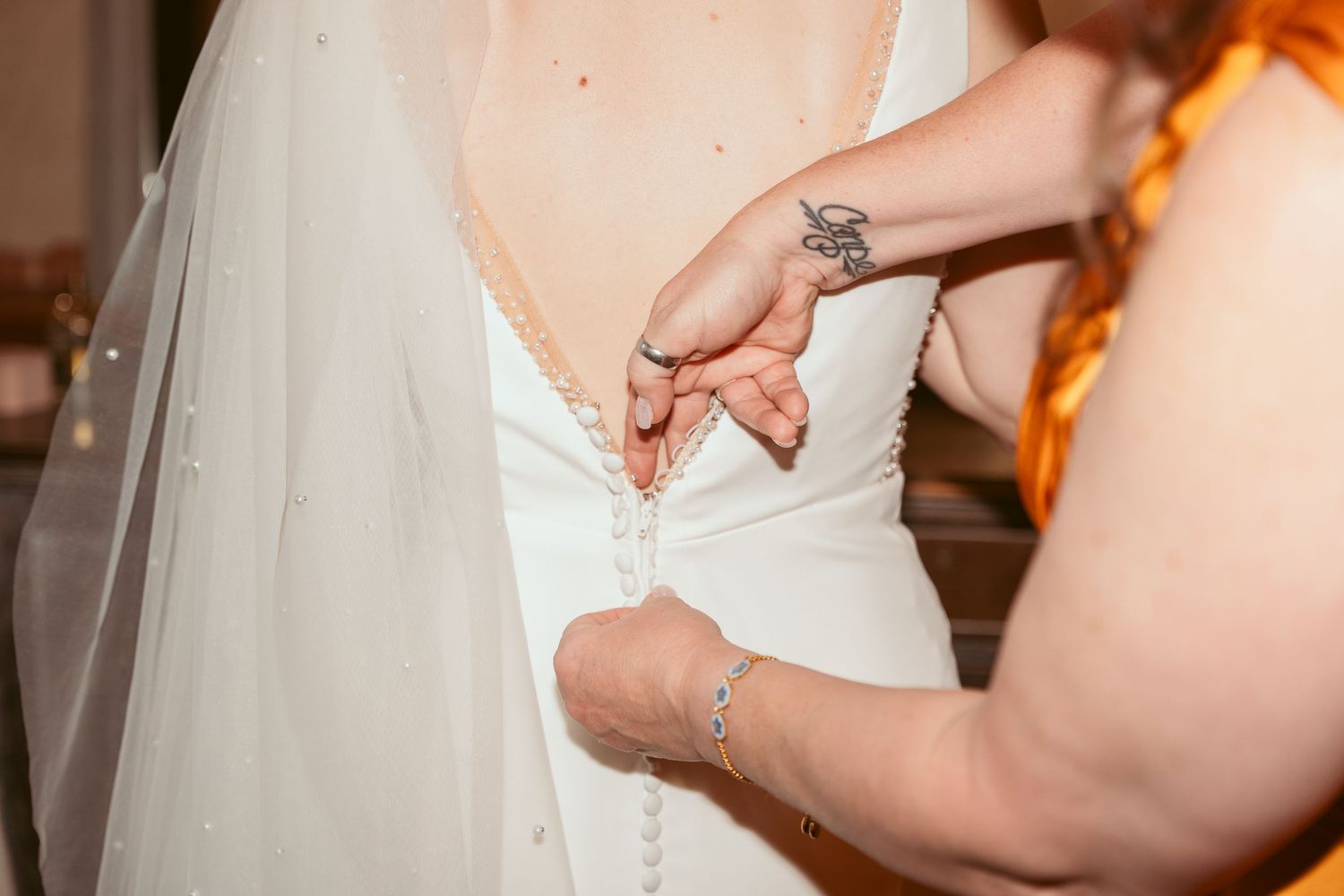 Close-up of wedding dress details being adjusted in rustic venue.