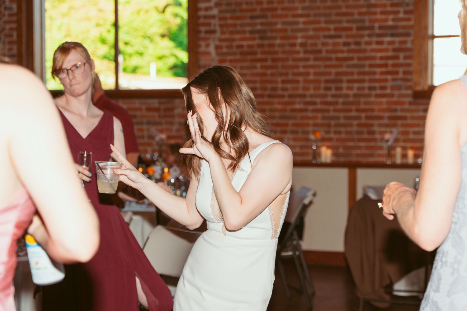 Guests dancing and celebrating at a wedding reception in a sunlit brick venue.