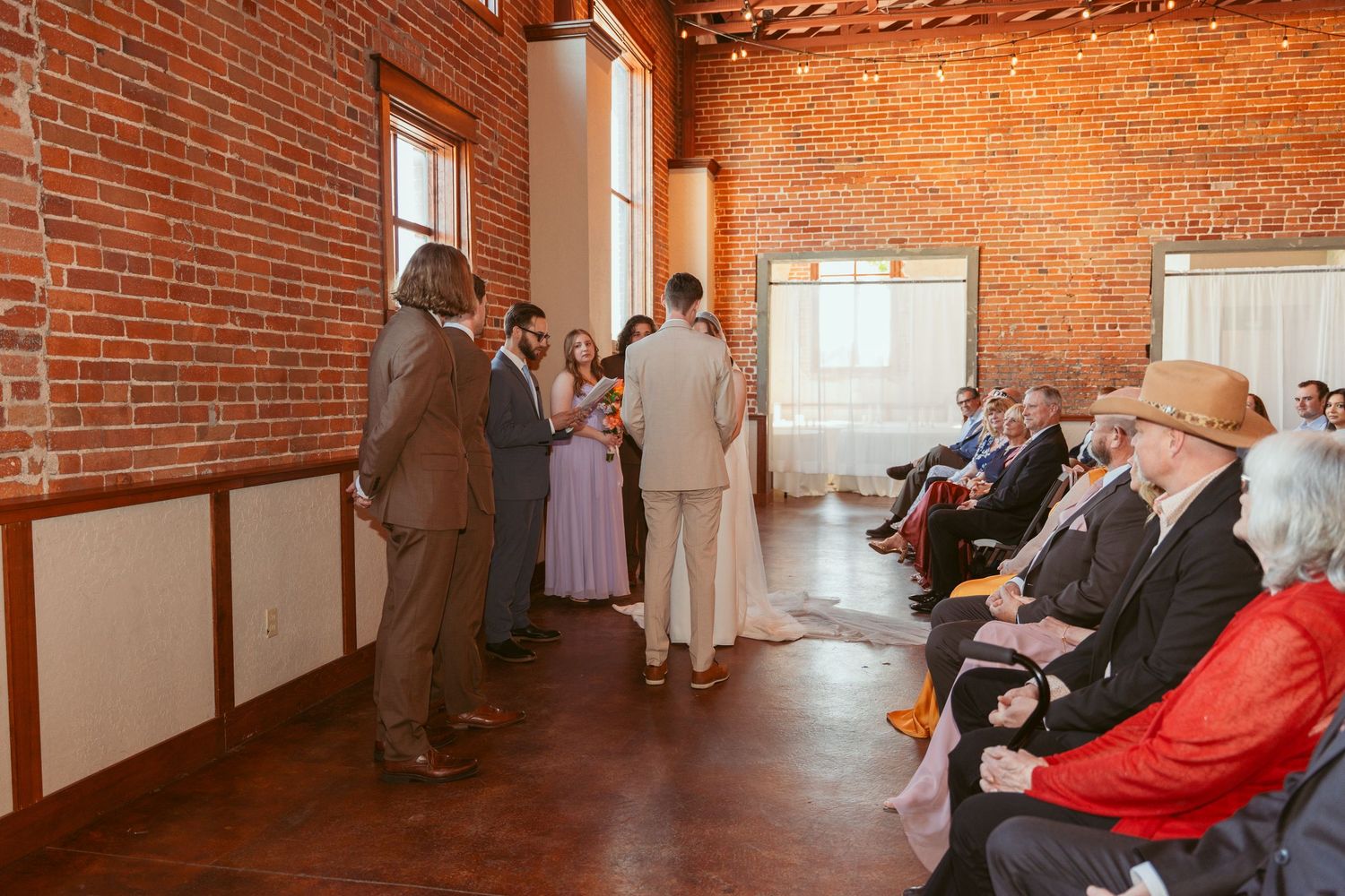 Wedding ceremony in a rustic brick venue with natural lighting streaming through windows.