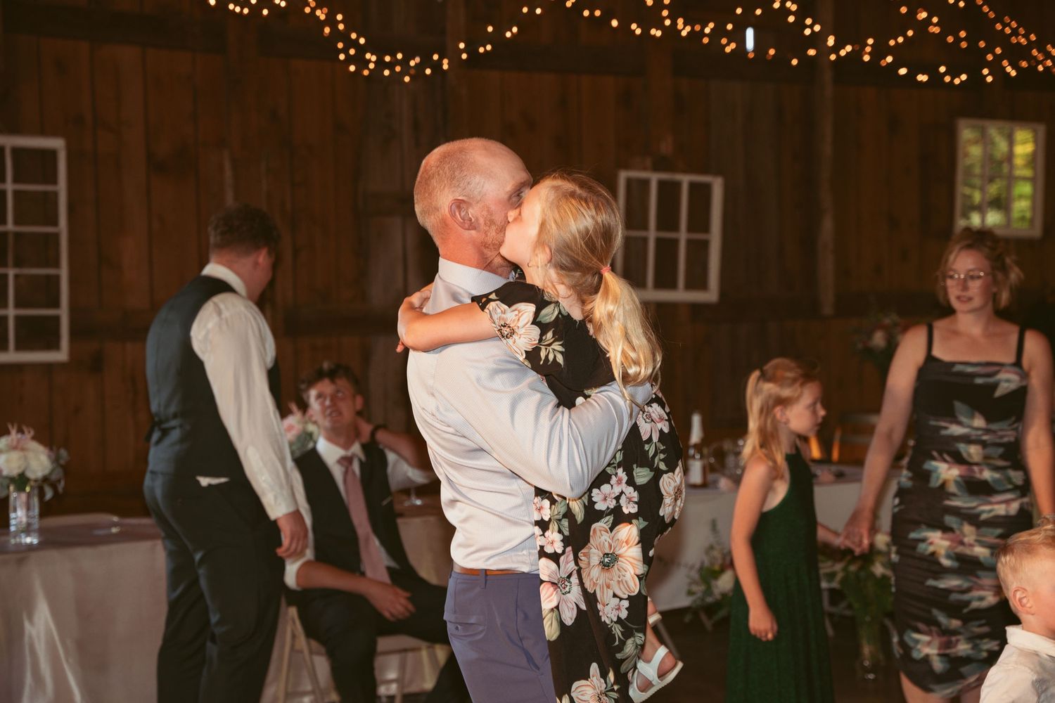 Couples slow dancing at an evening wedding reception under warm string lights.