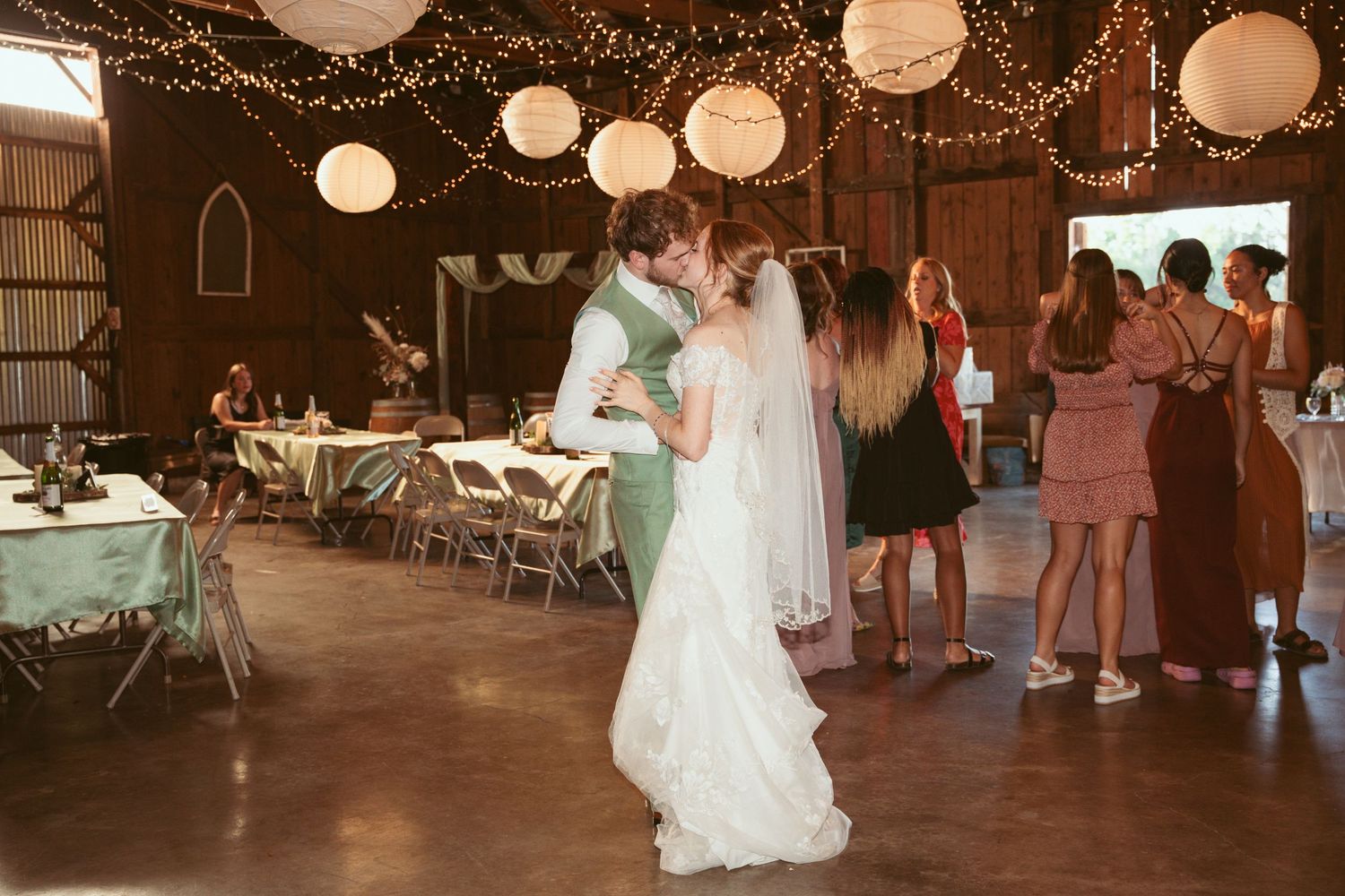 Wedding celebration in a rustic barn venue decorated with string lights and white paper lanterns.