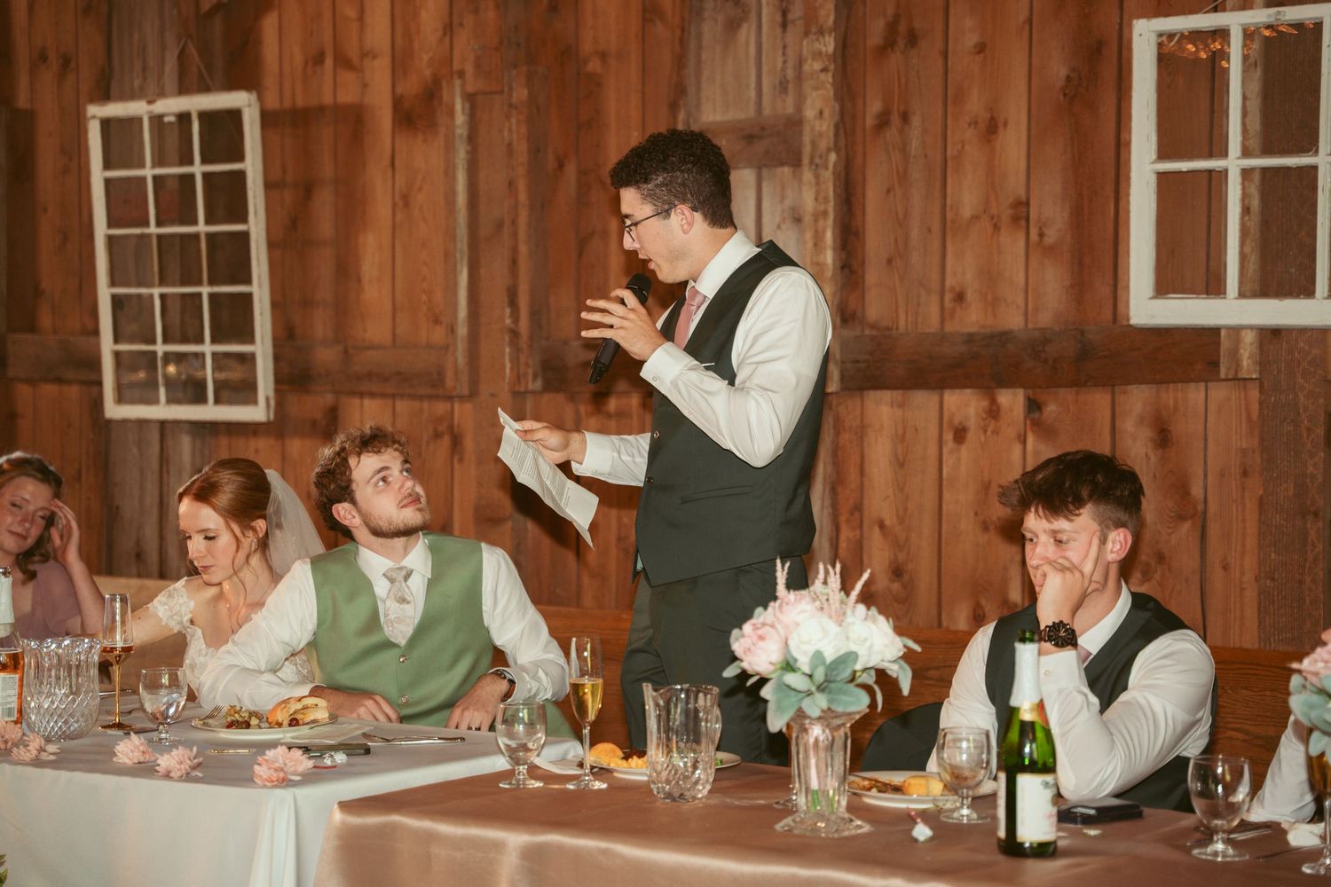 Emotional wedding toast being delivered at rustic barn reception with decorated tables.