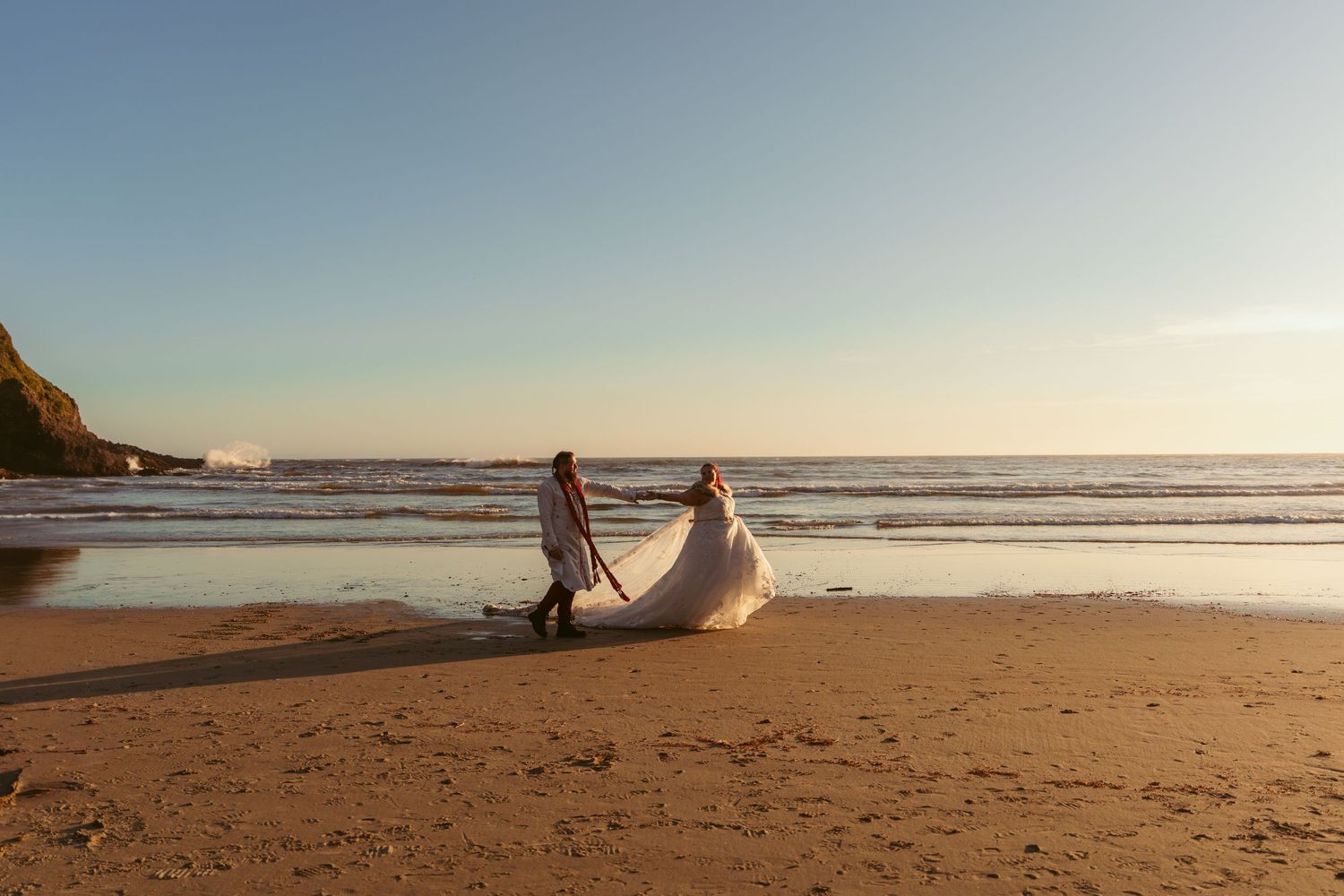 Wide view of sandy beach with cliffs and ocean waves at sunset.