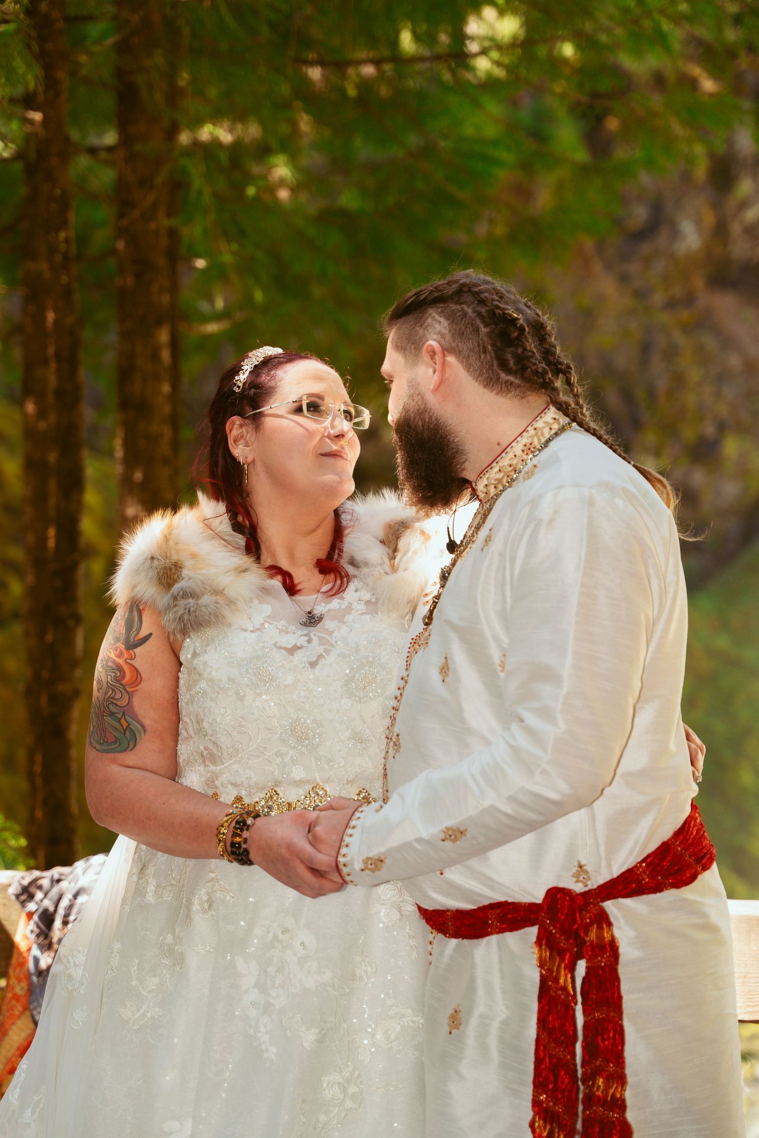A couple in Viking-inspired wedding attire share an intimate moment in a forest setting.