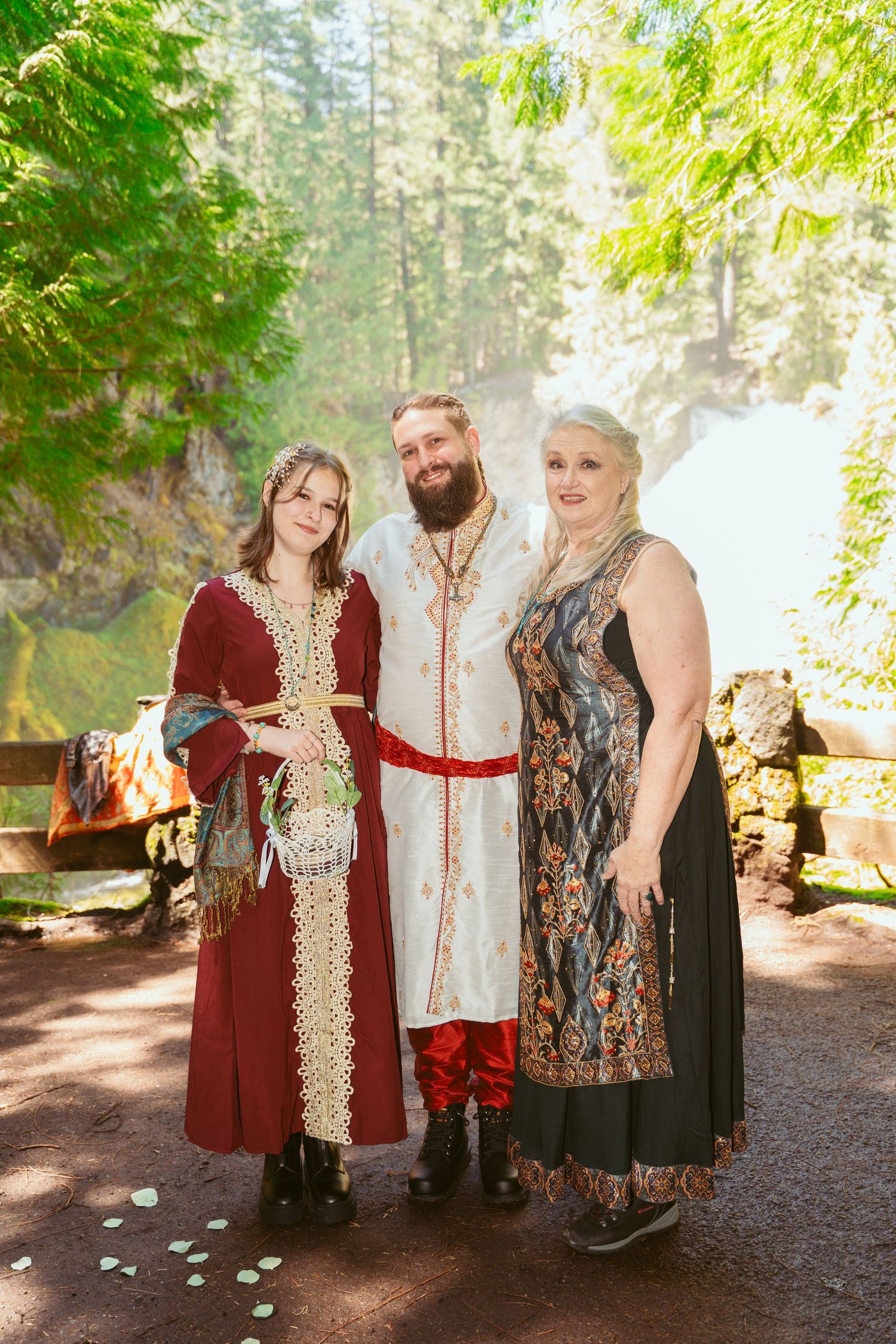 A group wearing medieval costumes poses together on a forest path with decorative outfits.