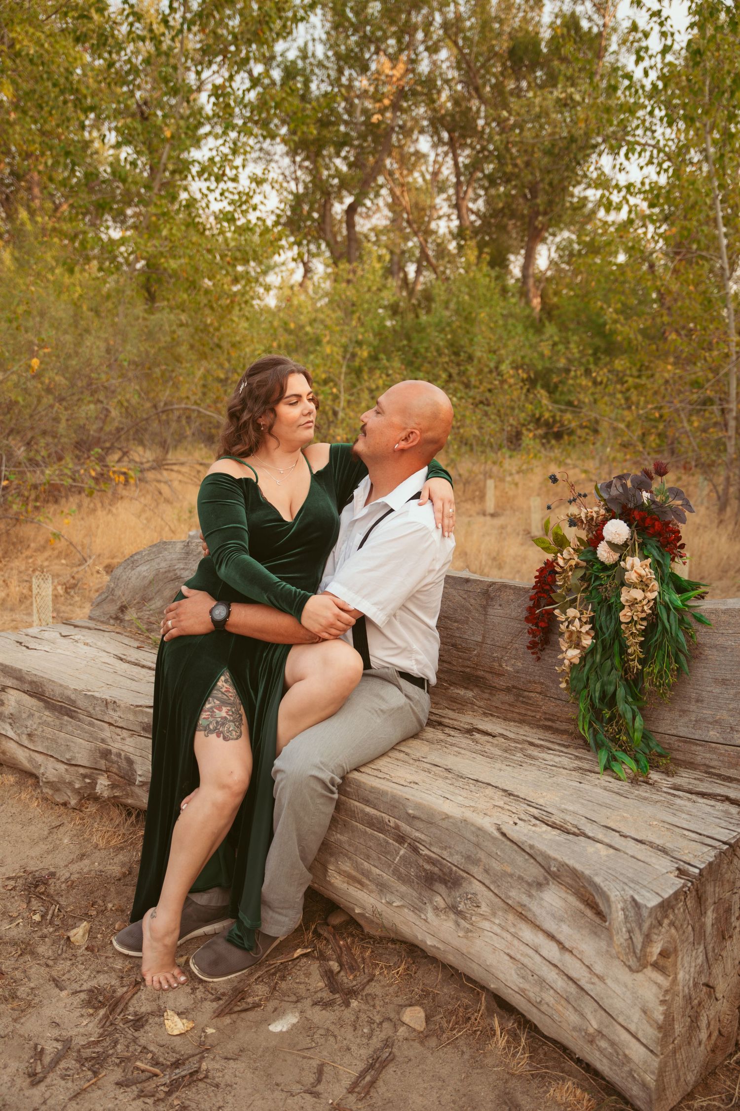 Couple in formal attire sharing intimate moments while posing on a fallen log by the water.