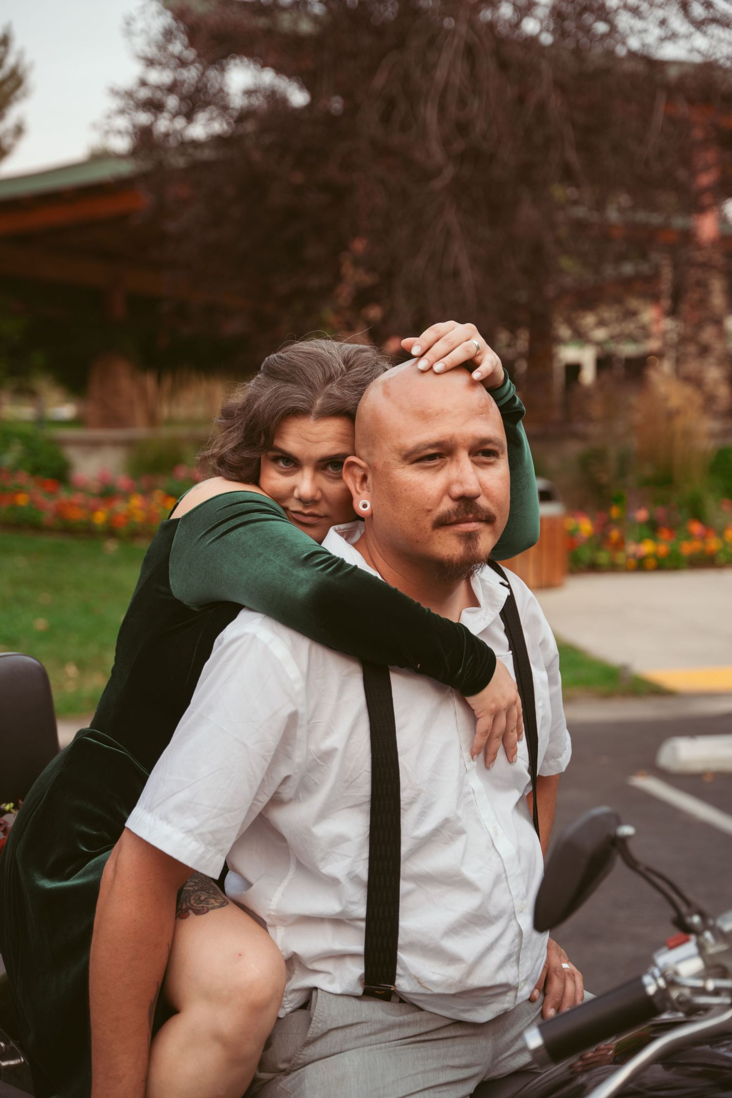 A couple shares a tender moment near a motorcycle in an autumn setting.