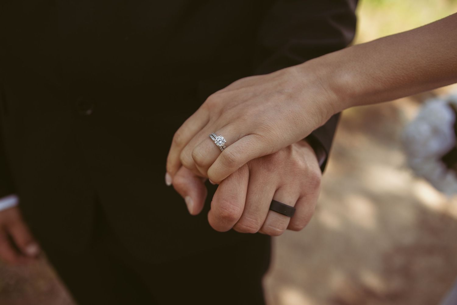 Close-up of clasped hands showing a sparkling engagement ring outdoors.