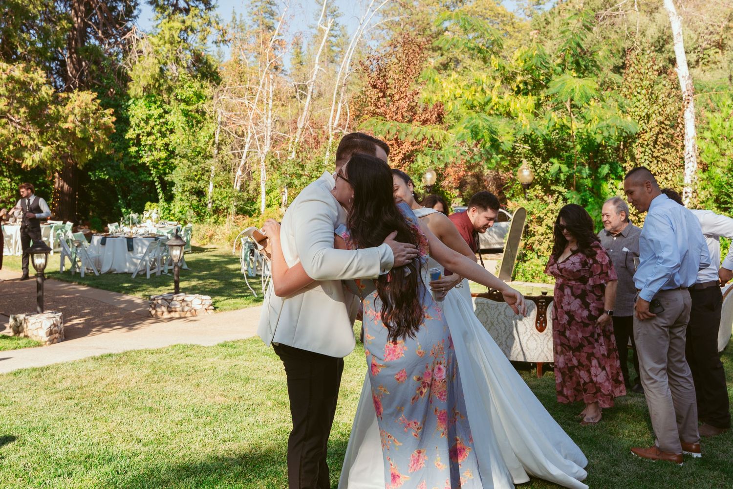 Outdoor wedding celebration in a garden setting with guests mingling during daytime.