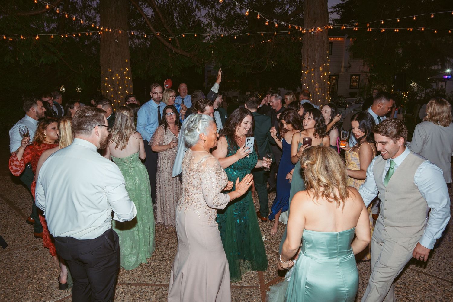 Wedding guests dancing under string lights at an outdoor evening reception.